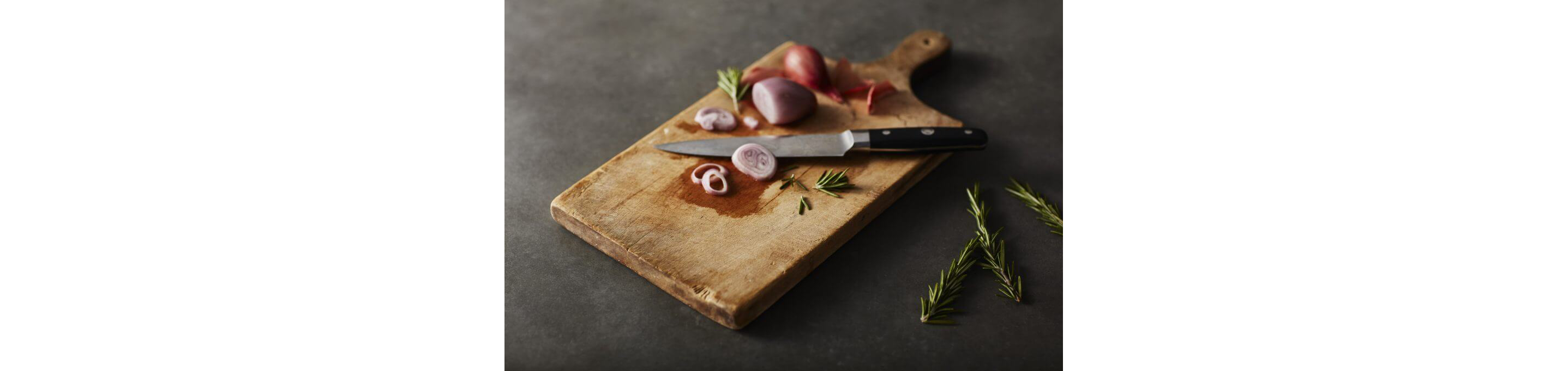 Sliced onions and thyme resting on a wooden cutting board.