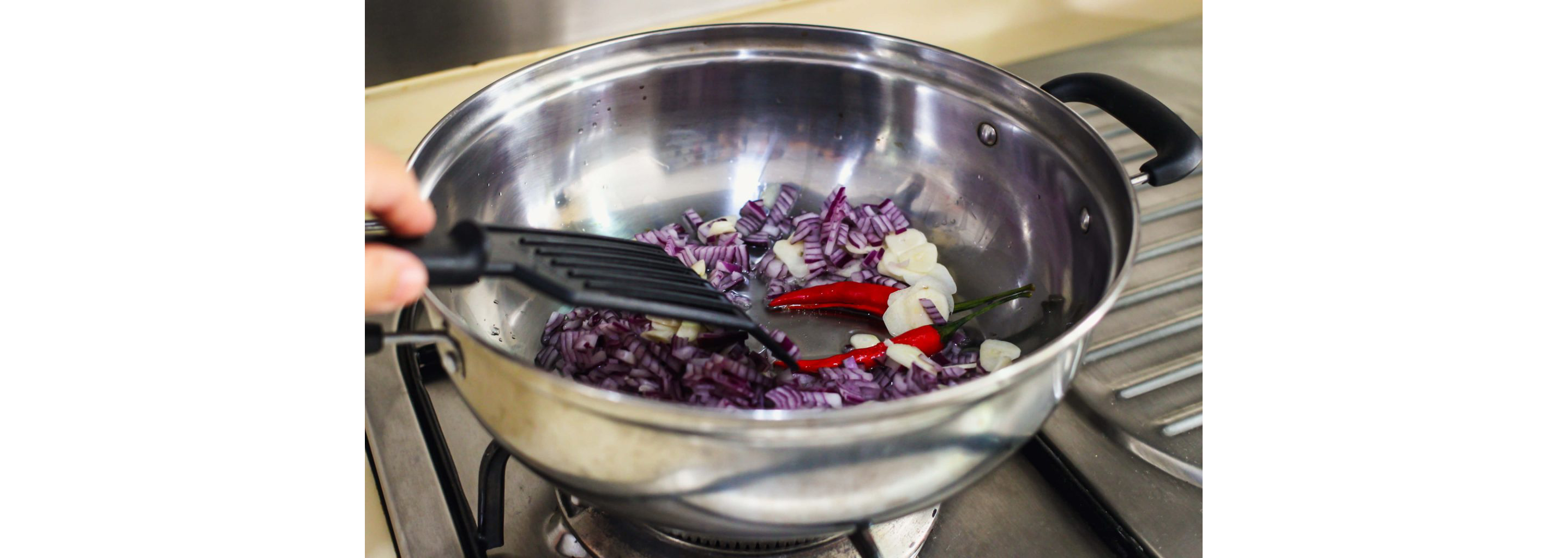 A pan sautéing diced red onion, garlic and peppers.