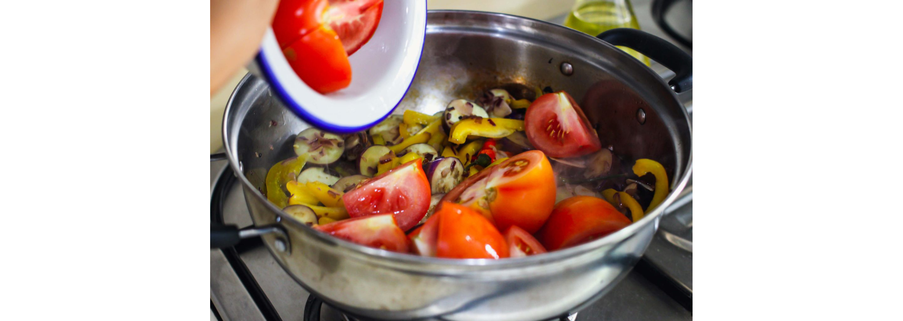 A large pot cooking sliced tomatoes, eggplant and more ingredients.