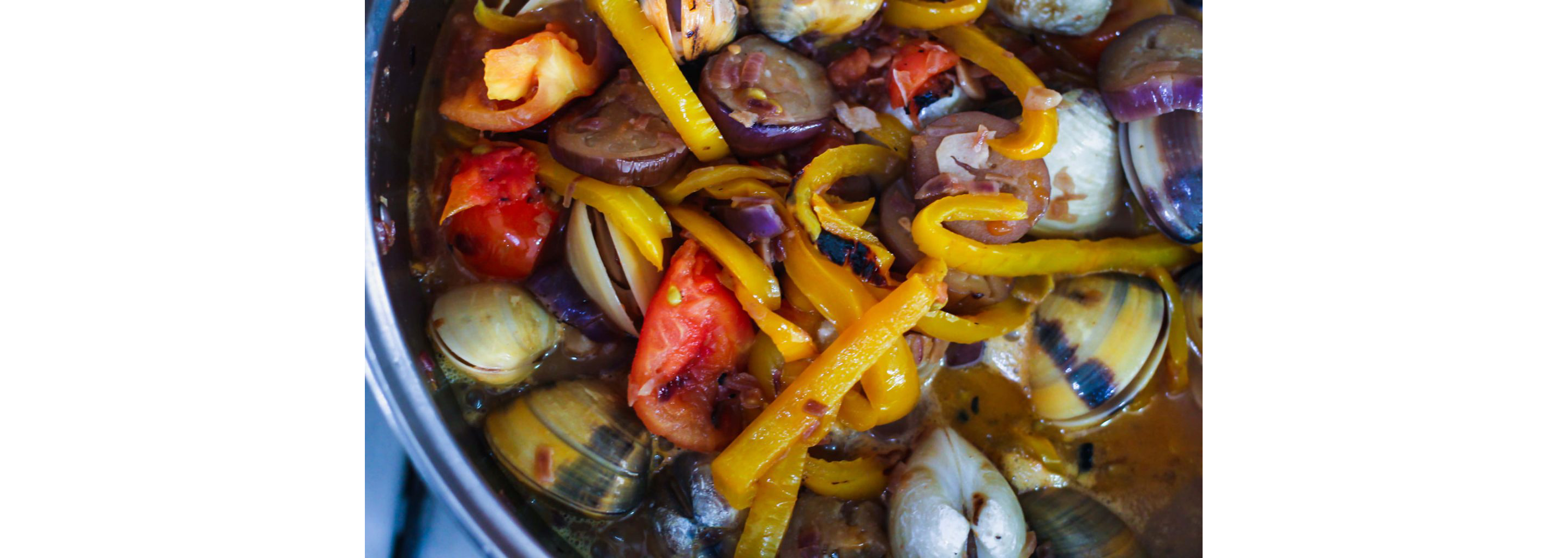 Clams, sliced peppers, eggplant and other ingredients boiling in a pot.
