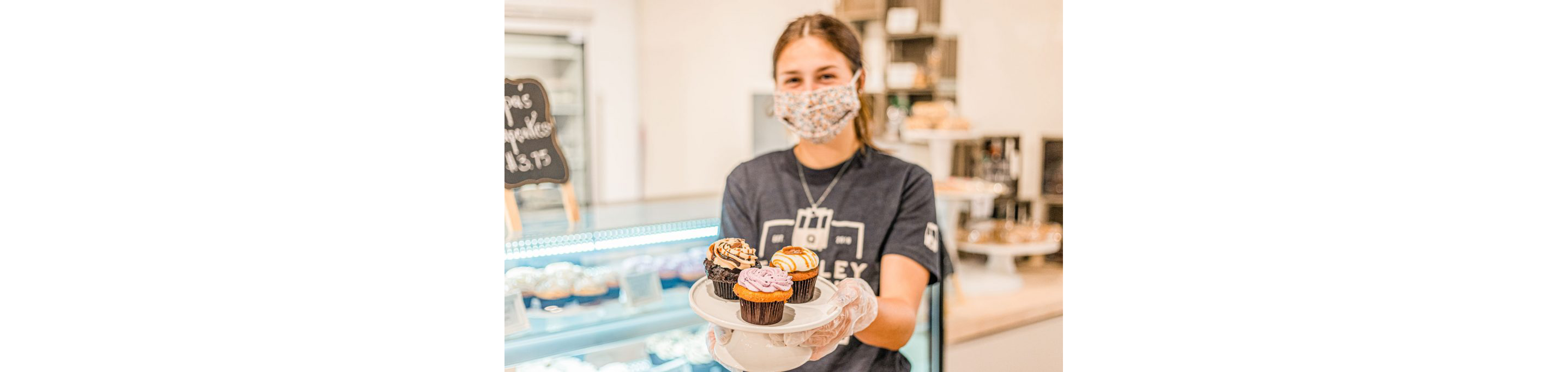 A person holding a small plate with three cupcakes.