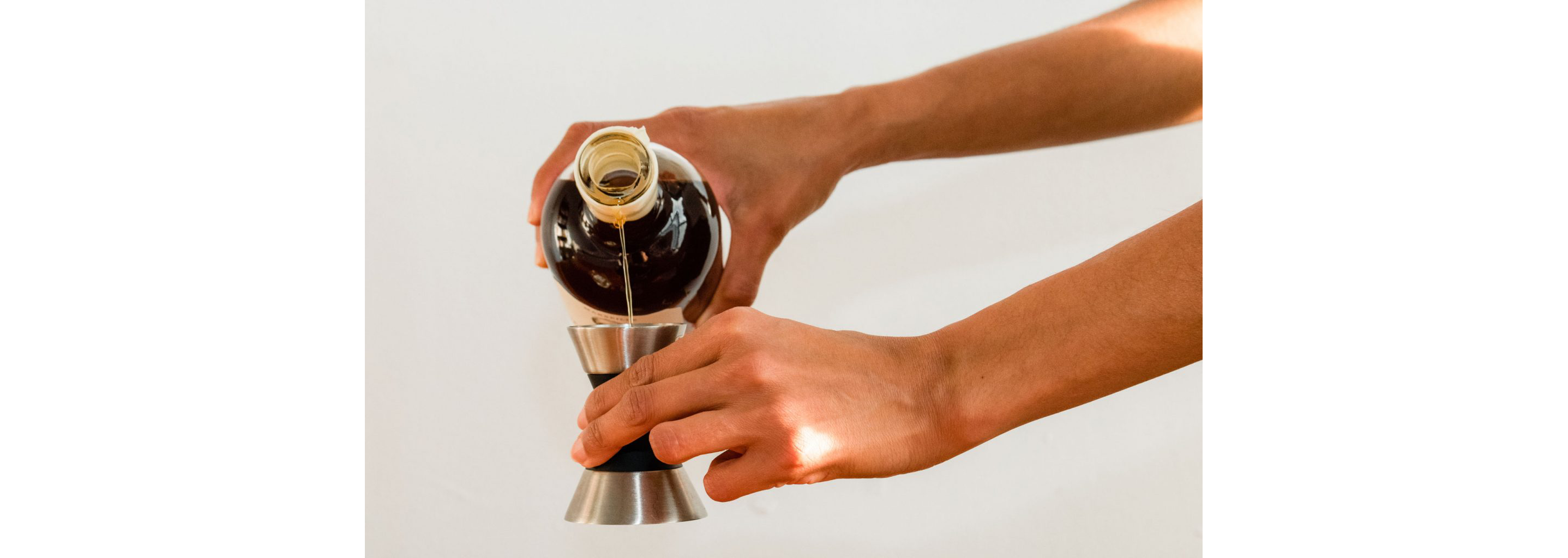 A person pouring Forthave Spirit liquor into a jigger.