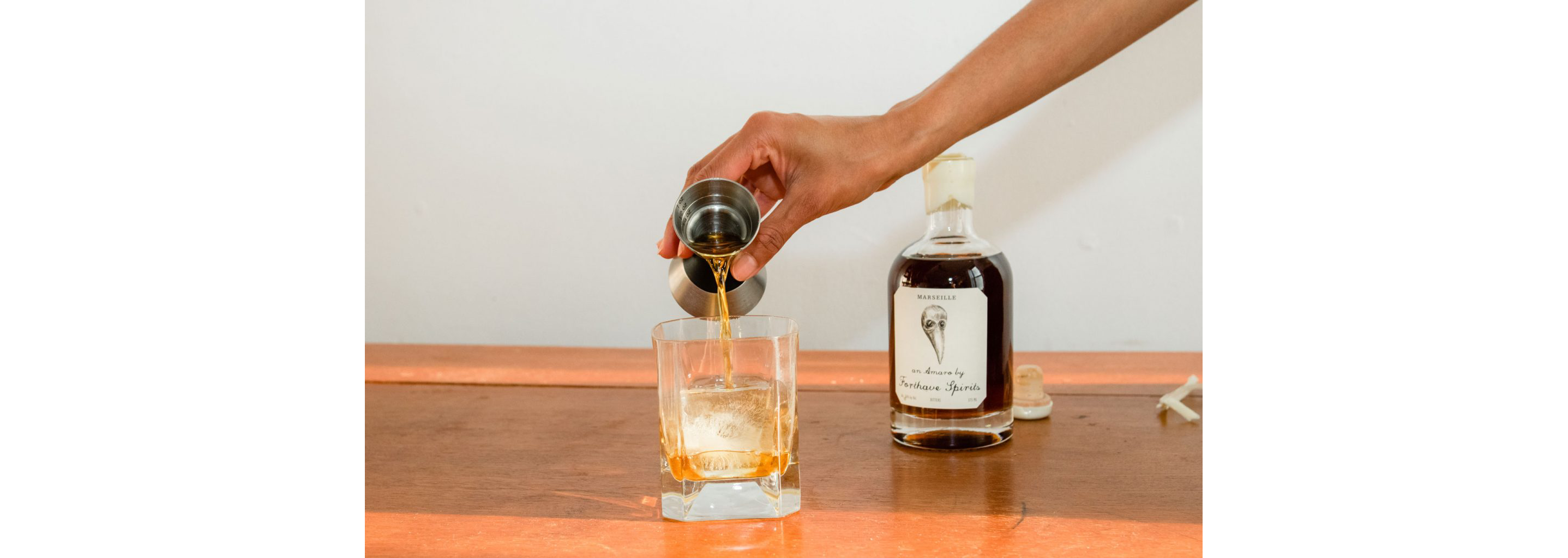 A person pouring Forthave Spirit liquor into a whiskey glass.
