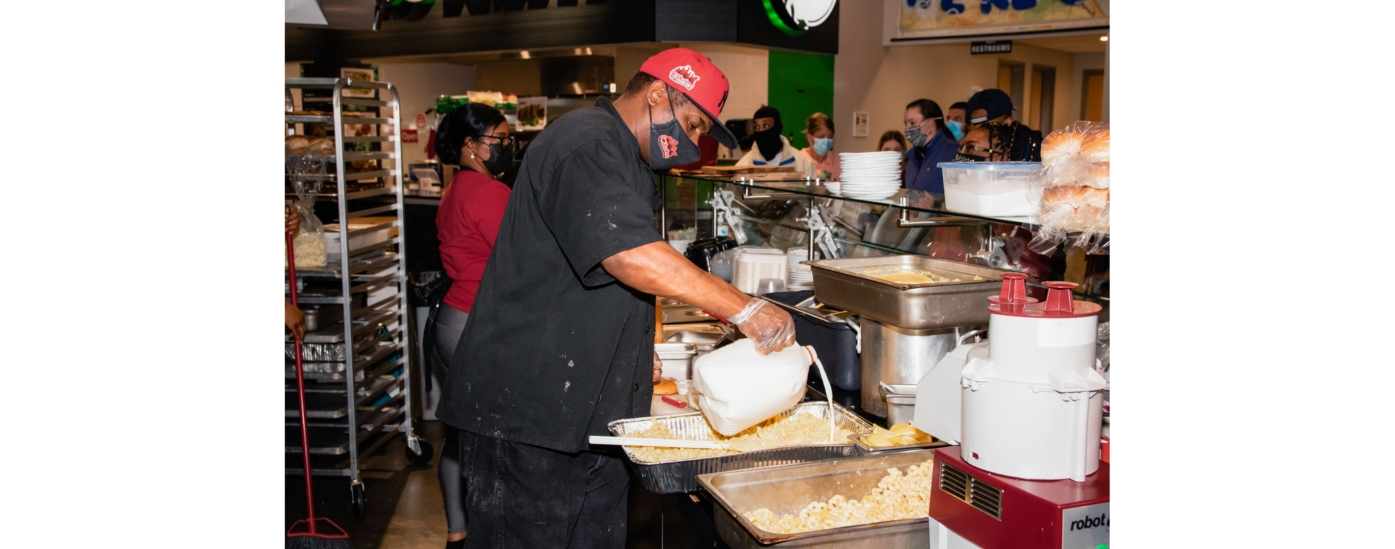 Sley adding milk to a large tray of mac and cheese.