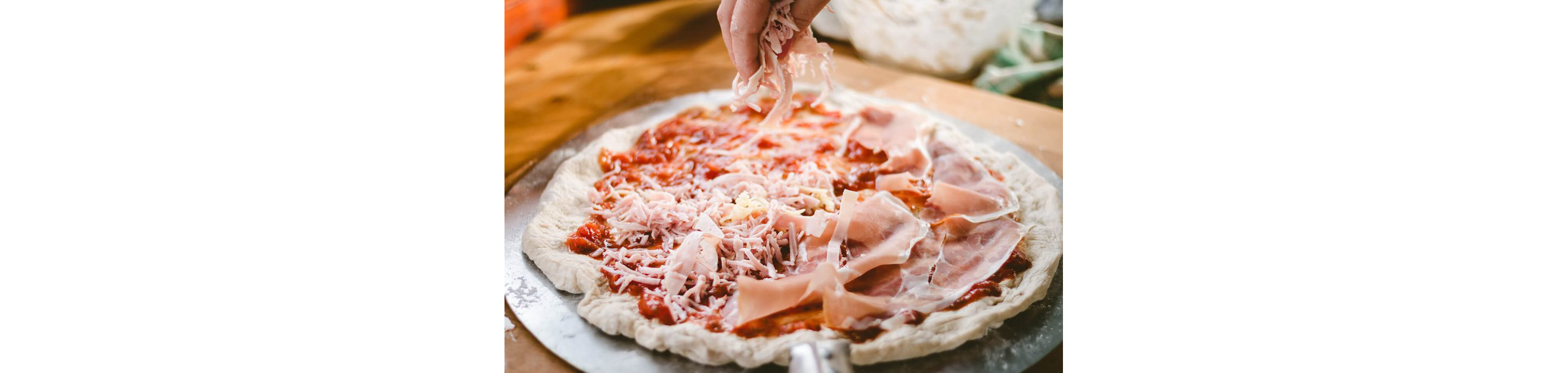 A person making a pizza from scratch, dressing it with sauce and other fixings.