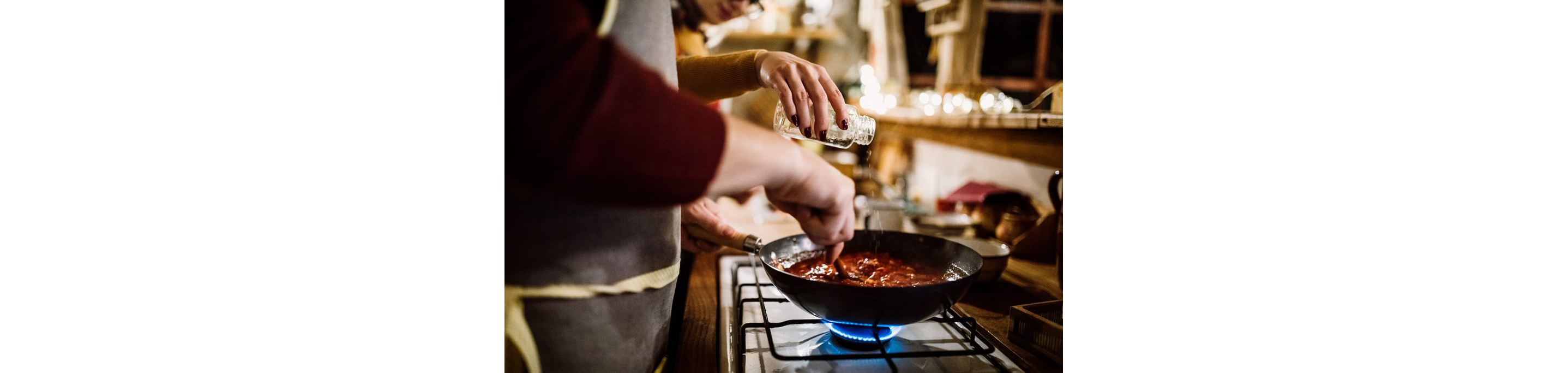 Two people cooking together as they prep sauce over the stove.
