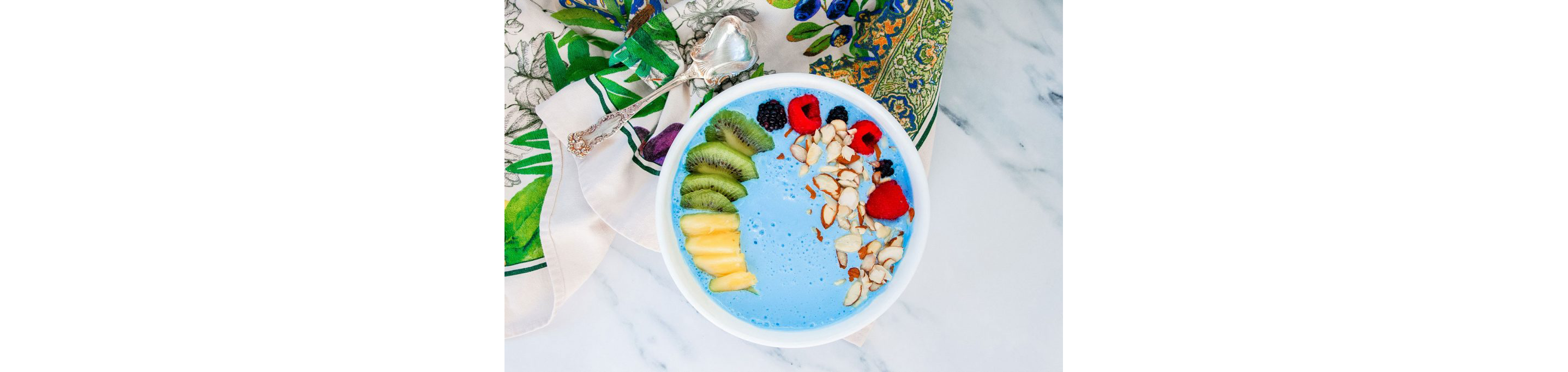 A blue smoothie bowl filled with sliced fruits and chopped nuts.
