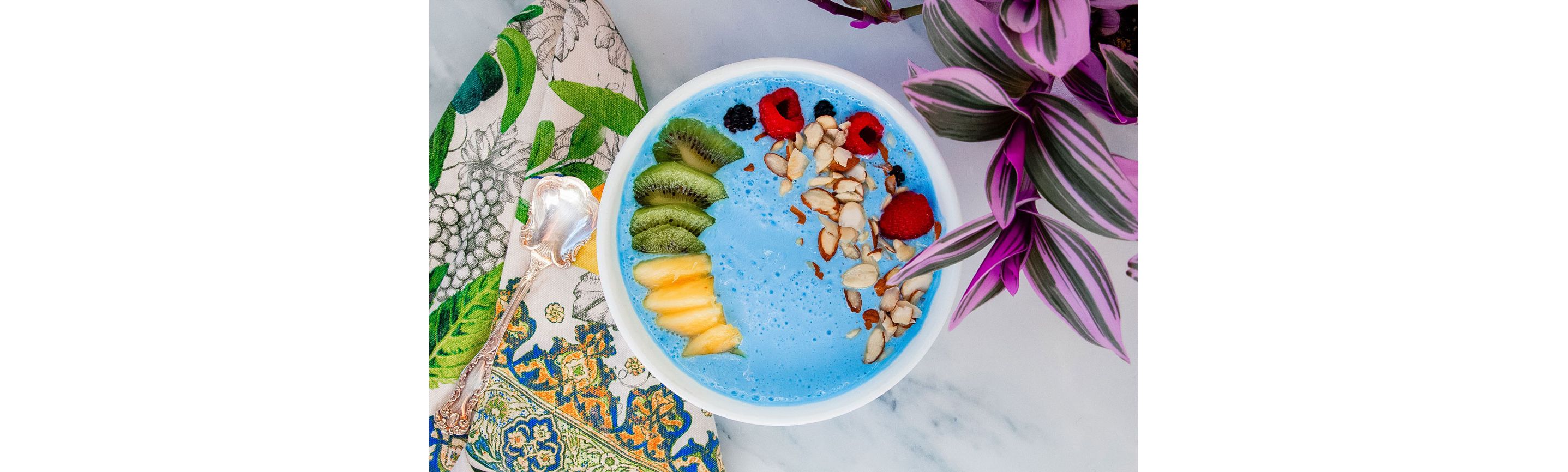 A blue smoothie bowl filled with sliced fruits and chopped nuts.