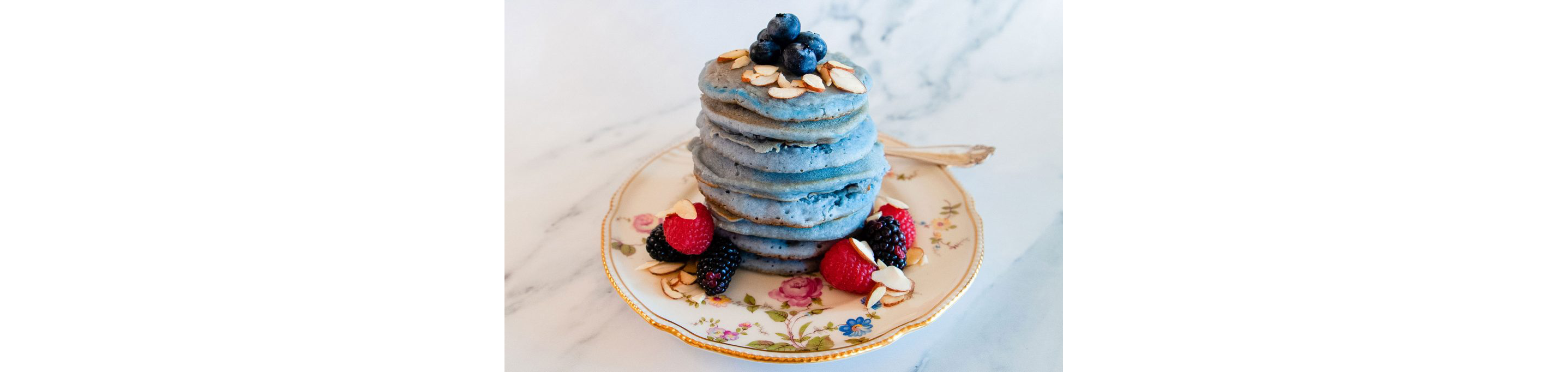 A small delicate plate towering with blue pancakes.