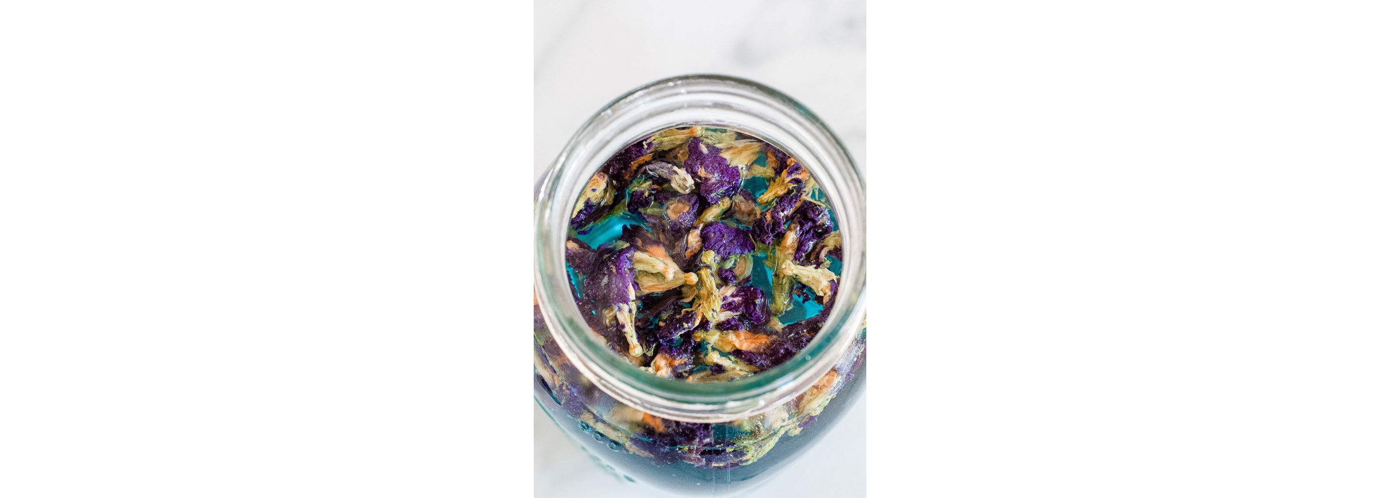 A glass jar filled with soaking butterfly pea flower petals.