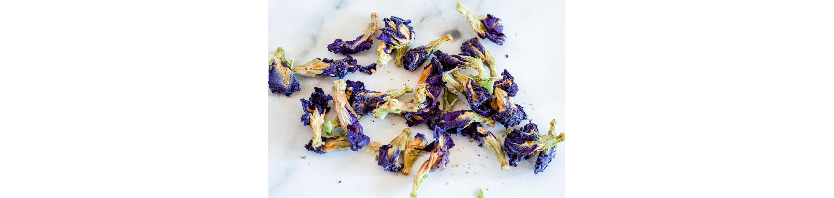 Dried butterfly pea flower petals scattered on a white table.