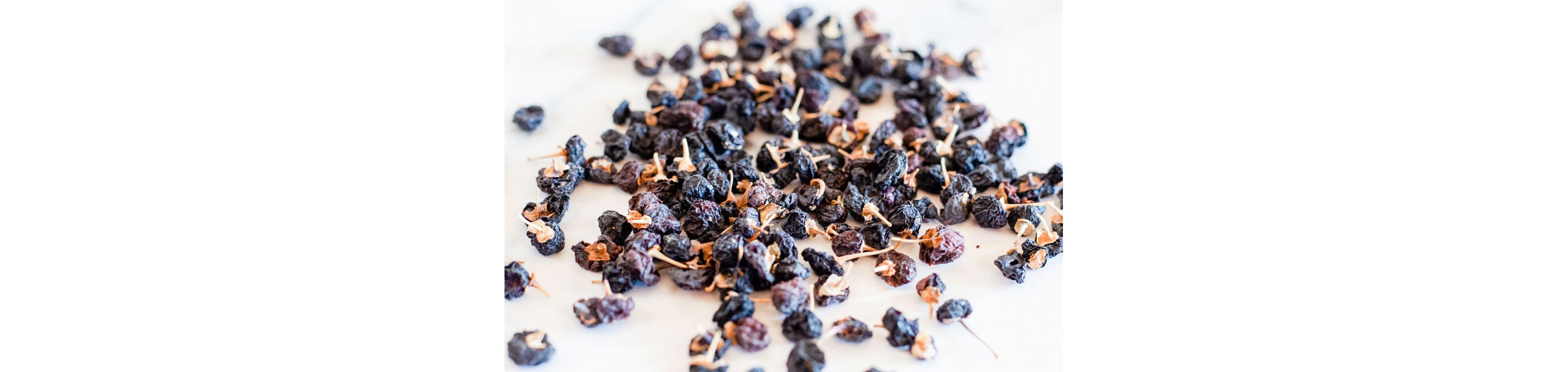 Dried black goji berries scattered across a white table.