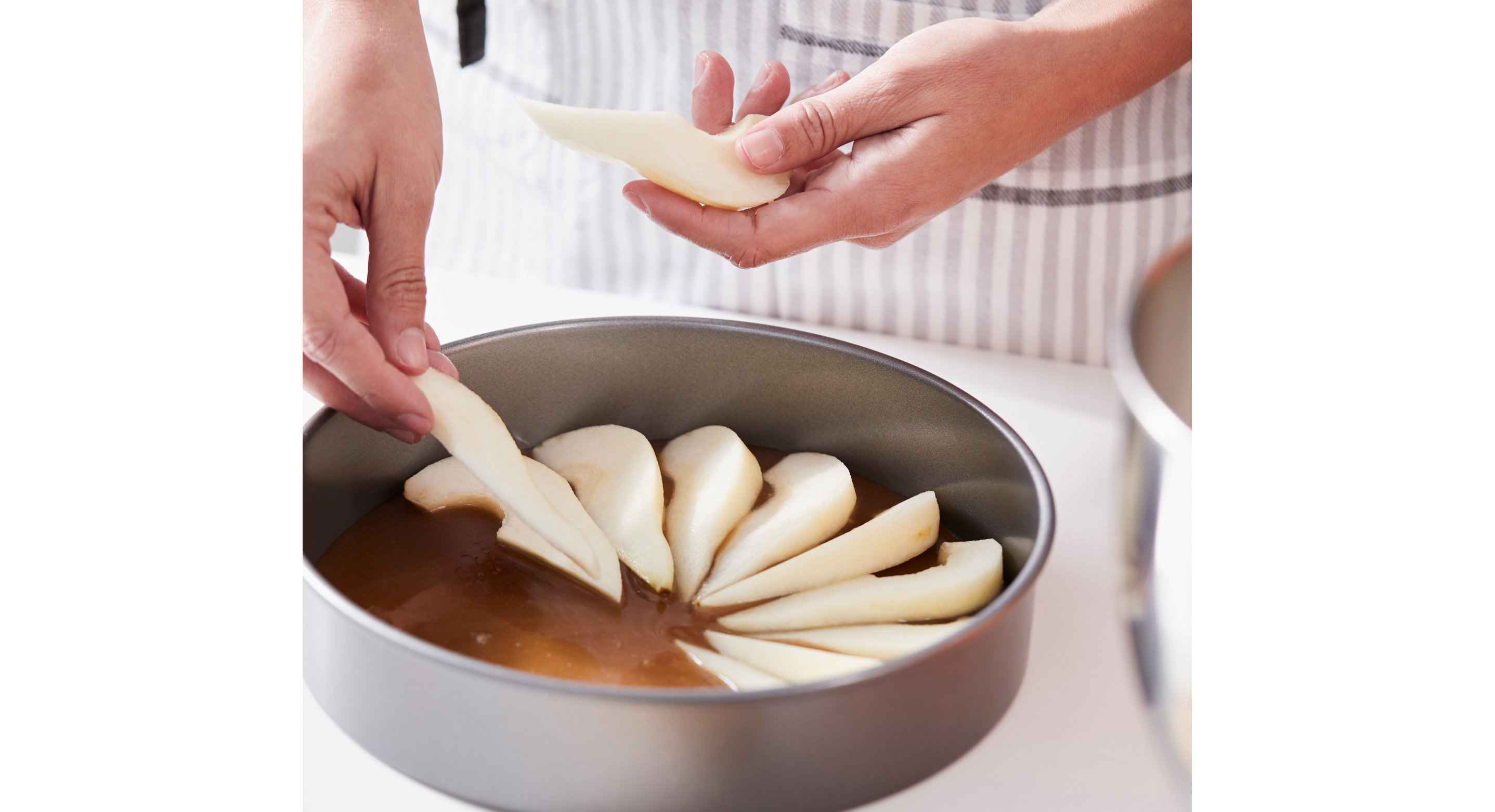 Person laying sliced pears in a cake tin