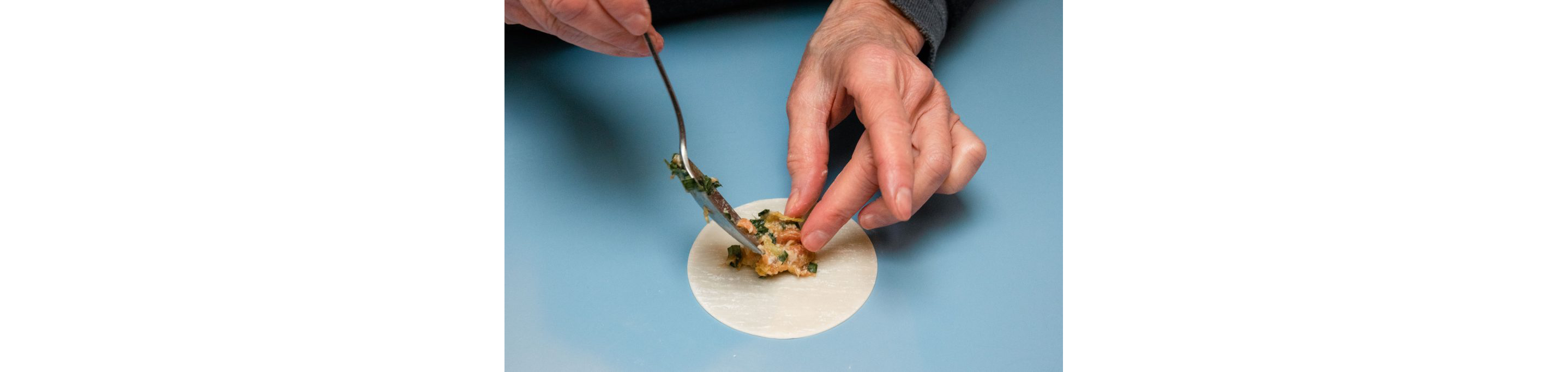 A person gently placing filling into a dumpling wrapper.