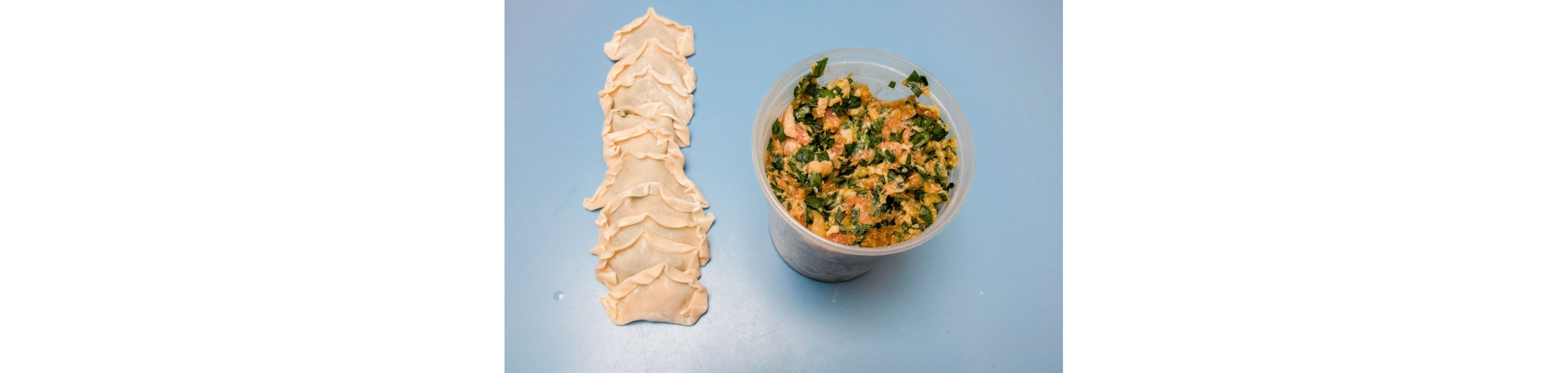 Freshly wrapped dumplings resting on the table next to a container of filling.