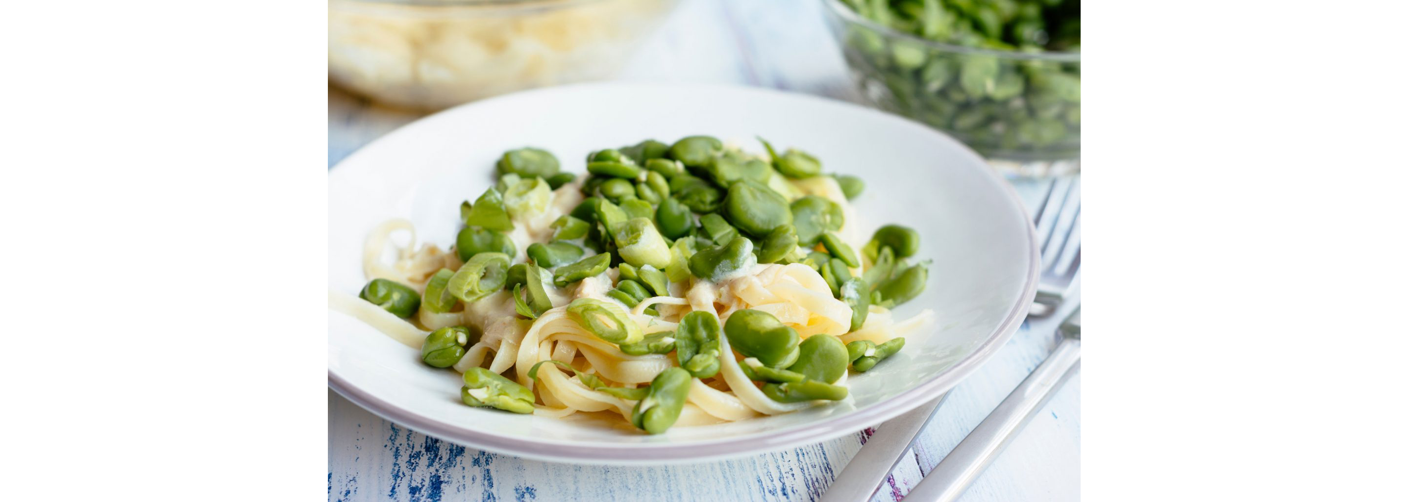 A white dish of spaghetti topped with fava beans.