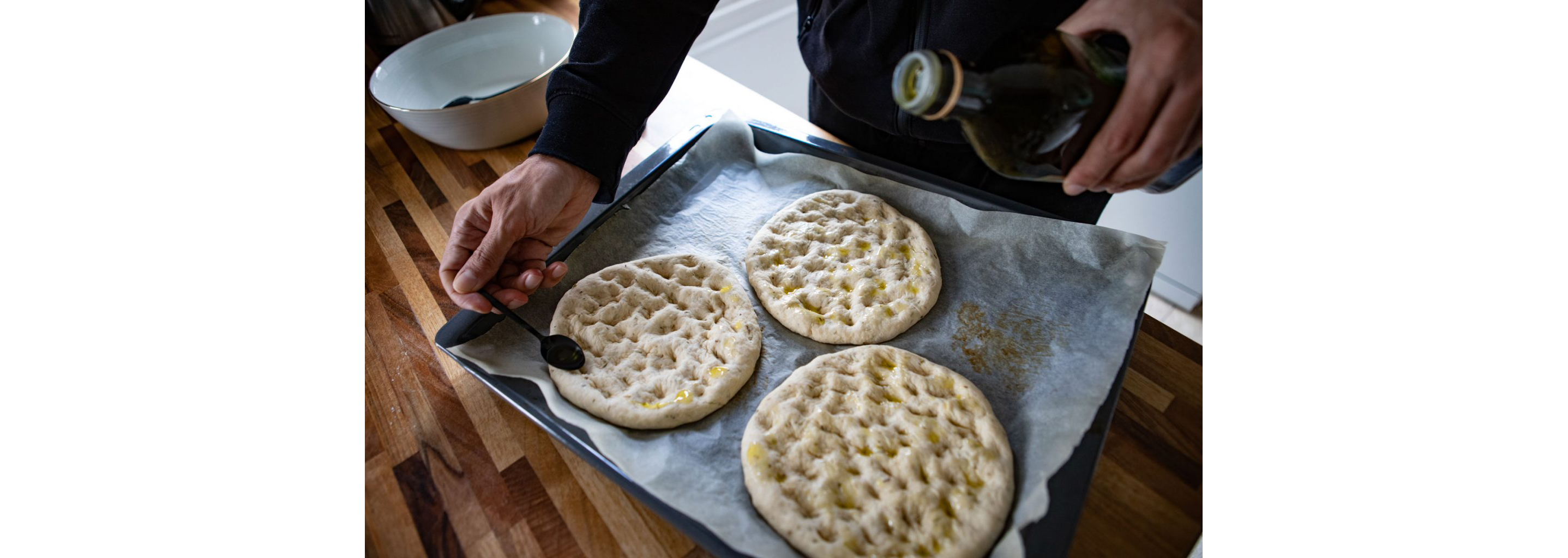 A person dressing focaccia bread with olive oil.