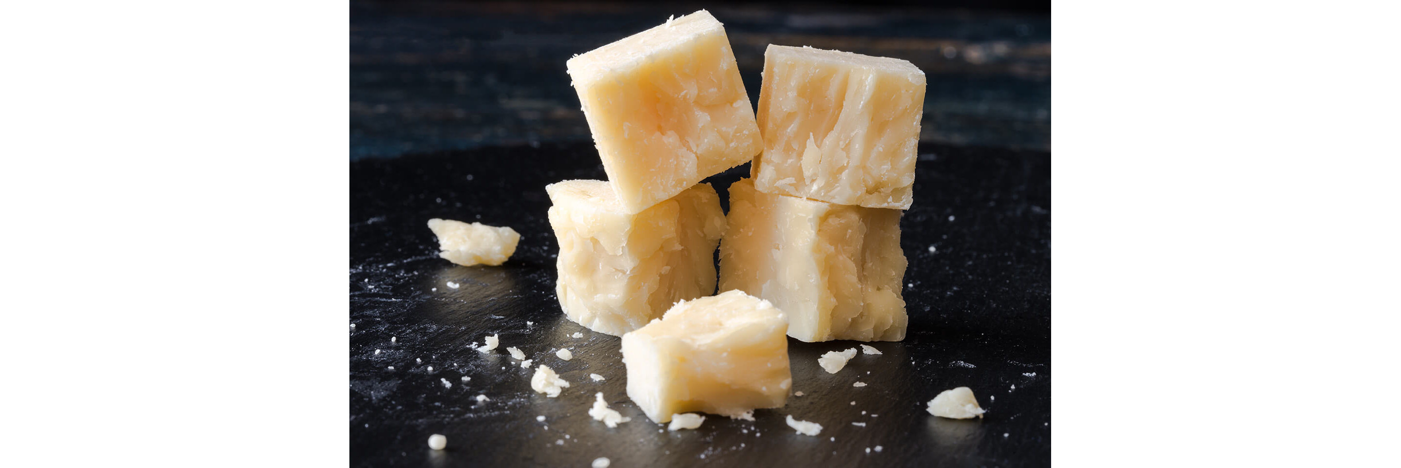 Crumbling cheese cut up into delicate cubes on a dark wooden cutting board.