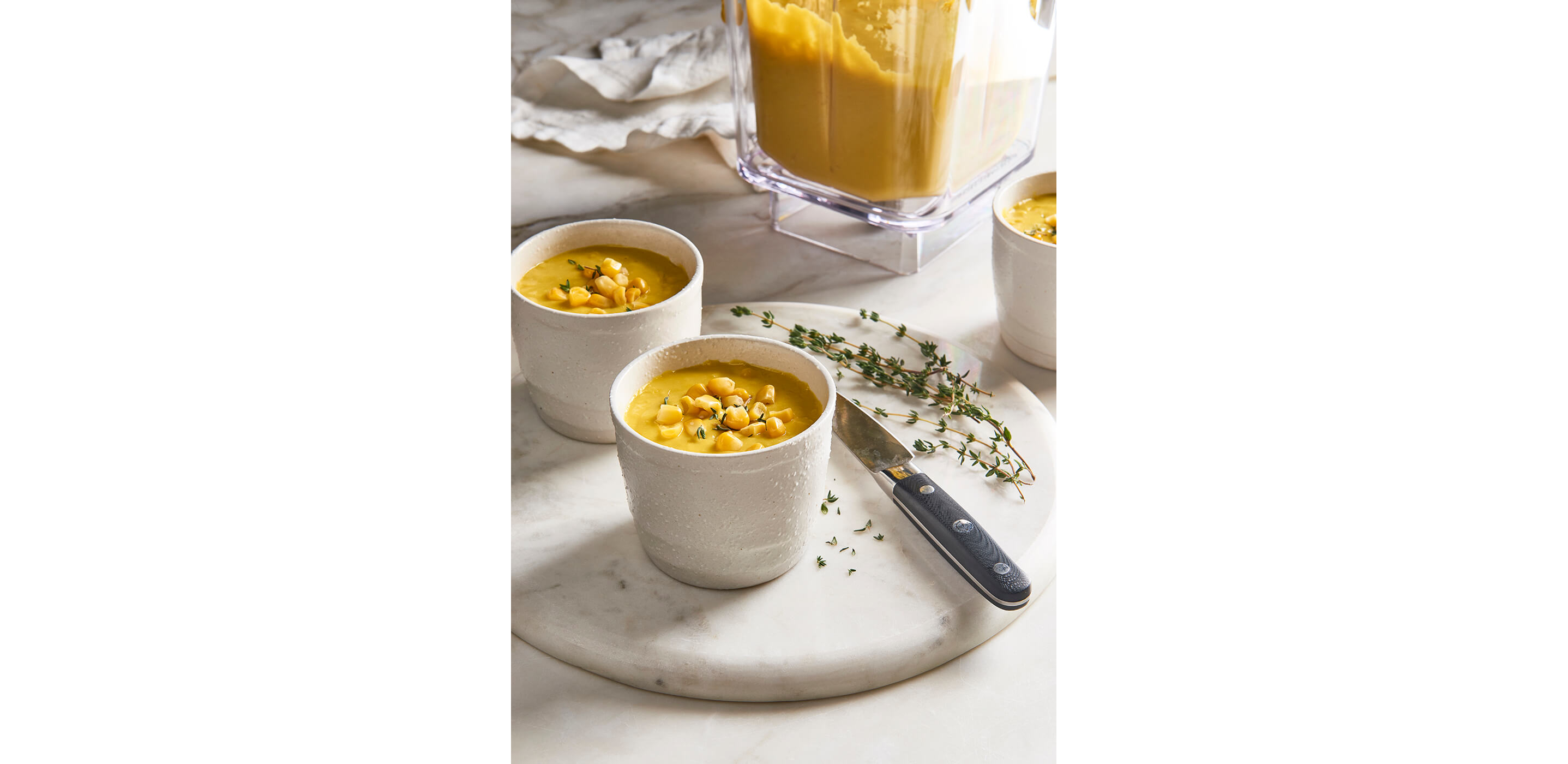 Two bowls of soup garnished with corn and thyme.