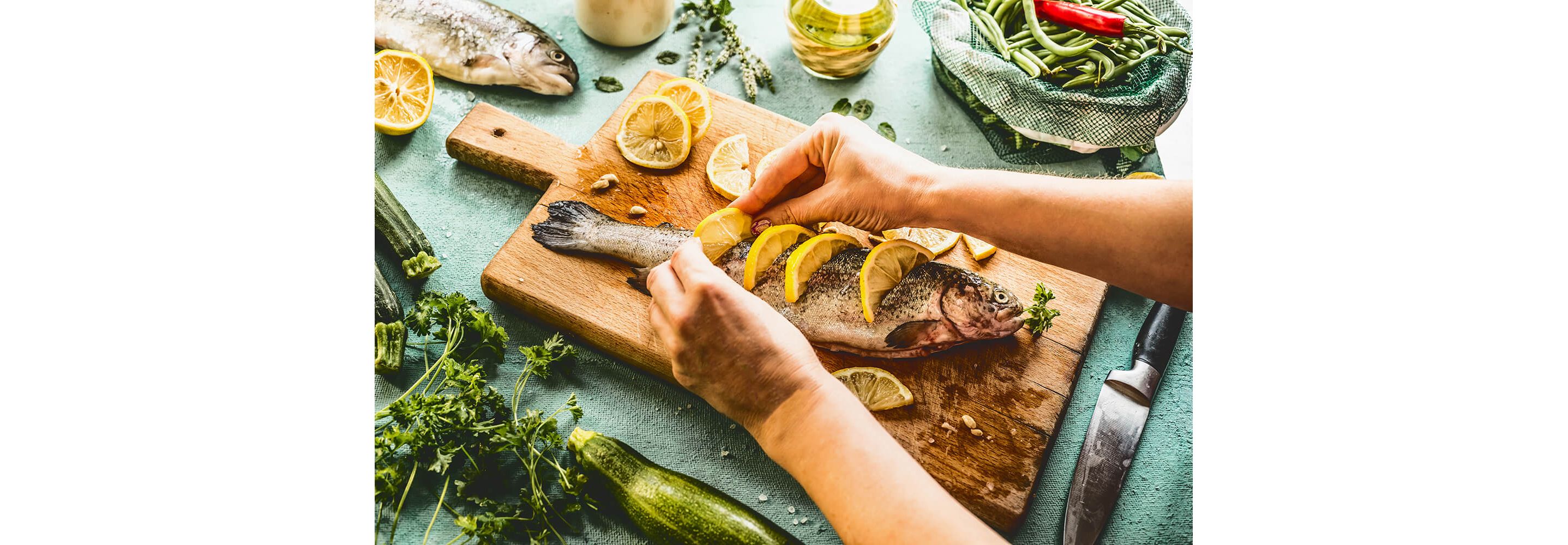 A whole fish laid down on a rustic wooden cutting board garnished with sliced lemons.