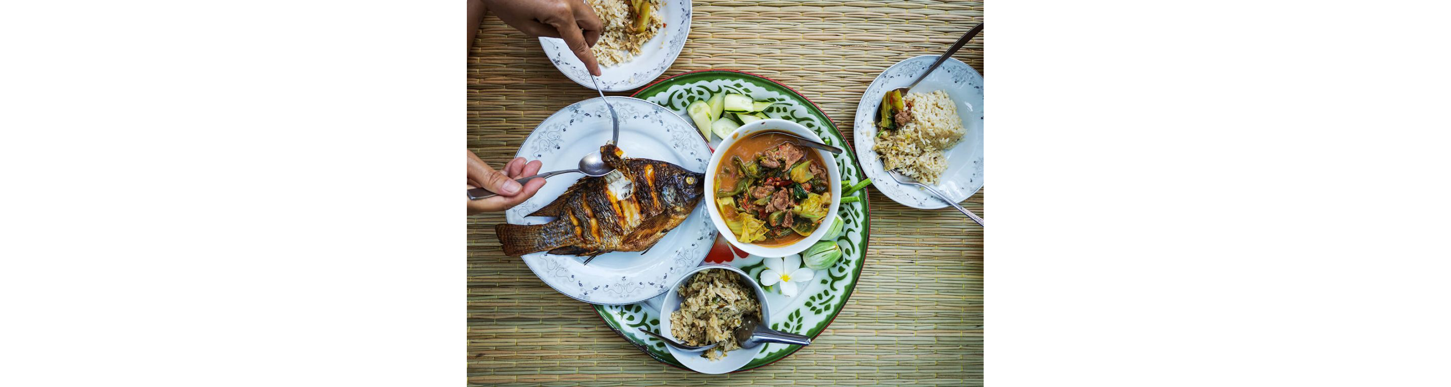 A roasted whole fish resting on a white plate accompanied by curry, rice and vegetables.