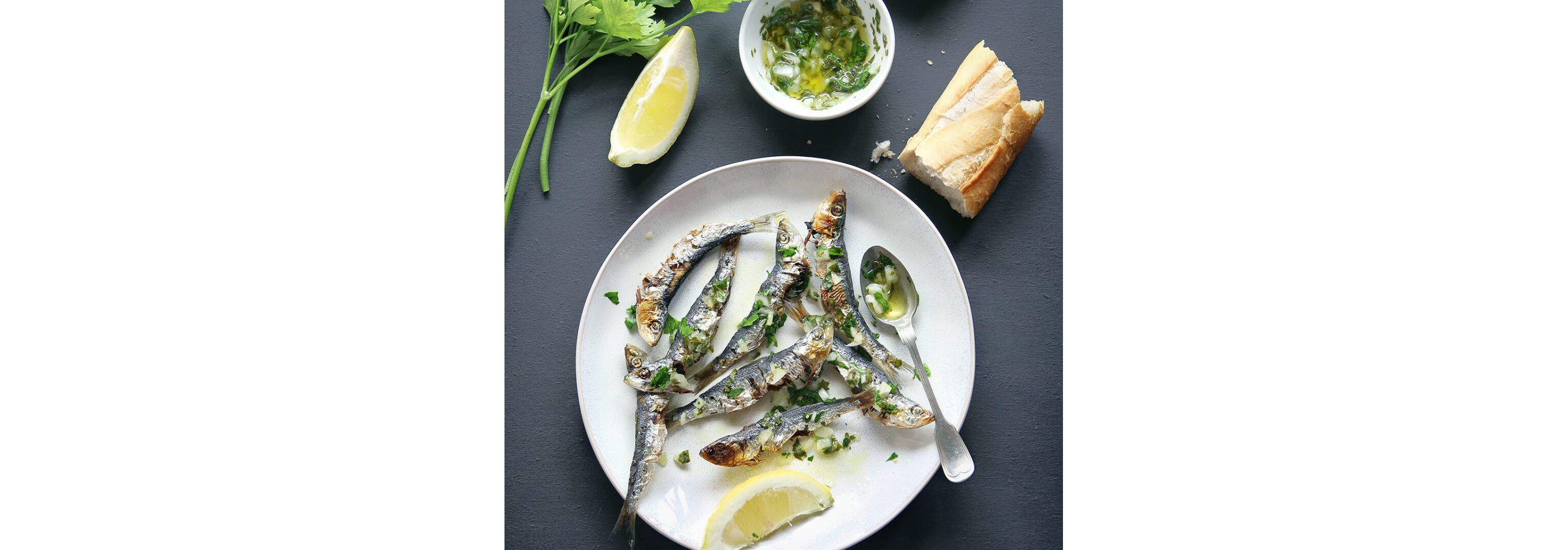 Roasted sardines on a clean white plate garnished with sliced lemons and cilantro.