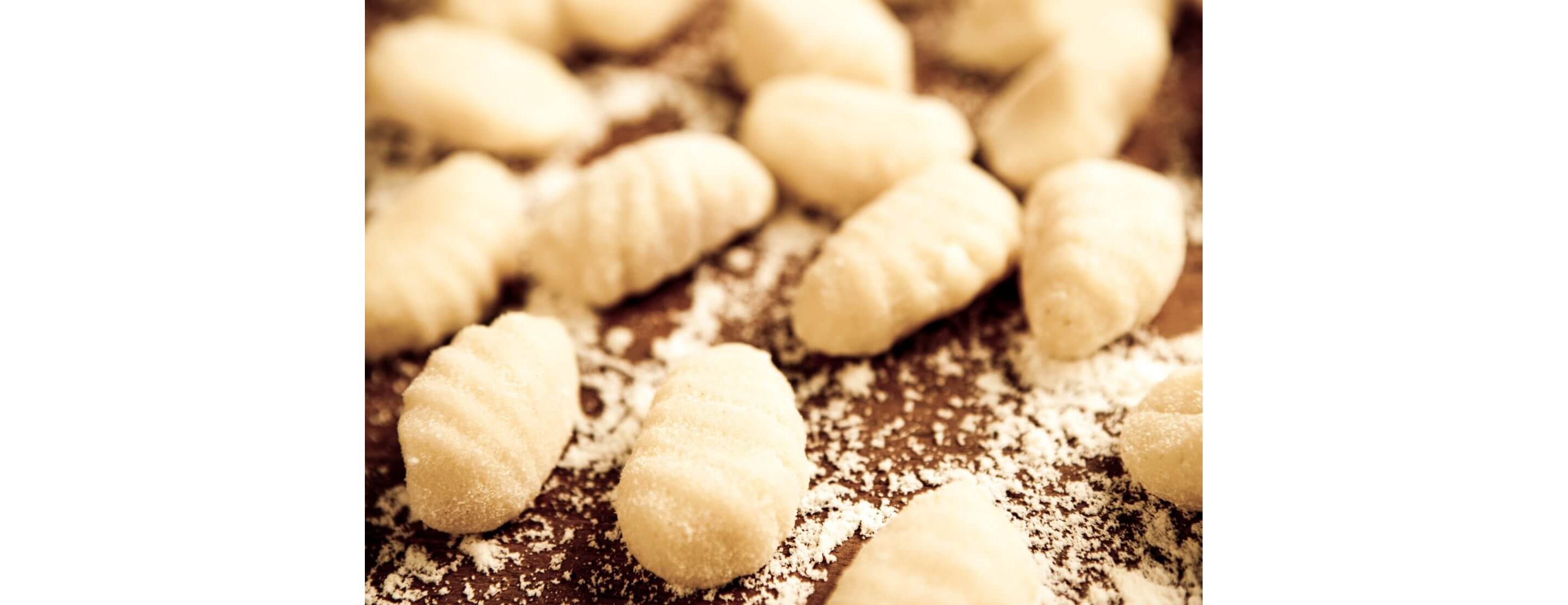 Handmade gnocchi coated in flour resting on a wooden cutting board.