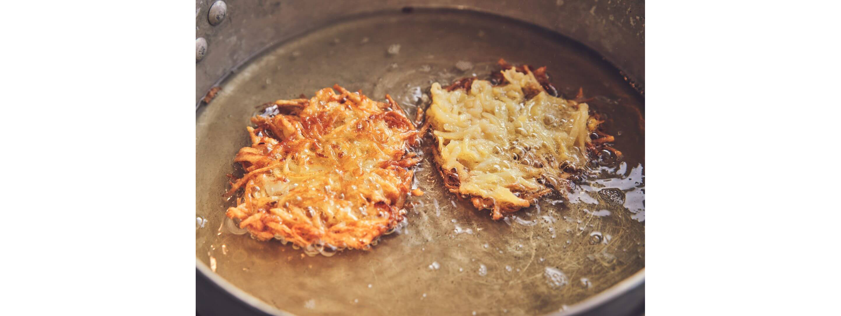 Two potato pancakes decadently frying in a pan of glistening oil.