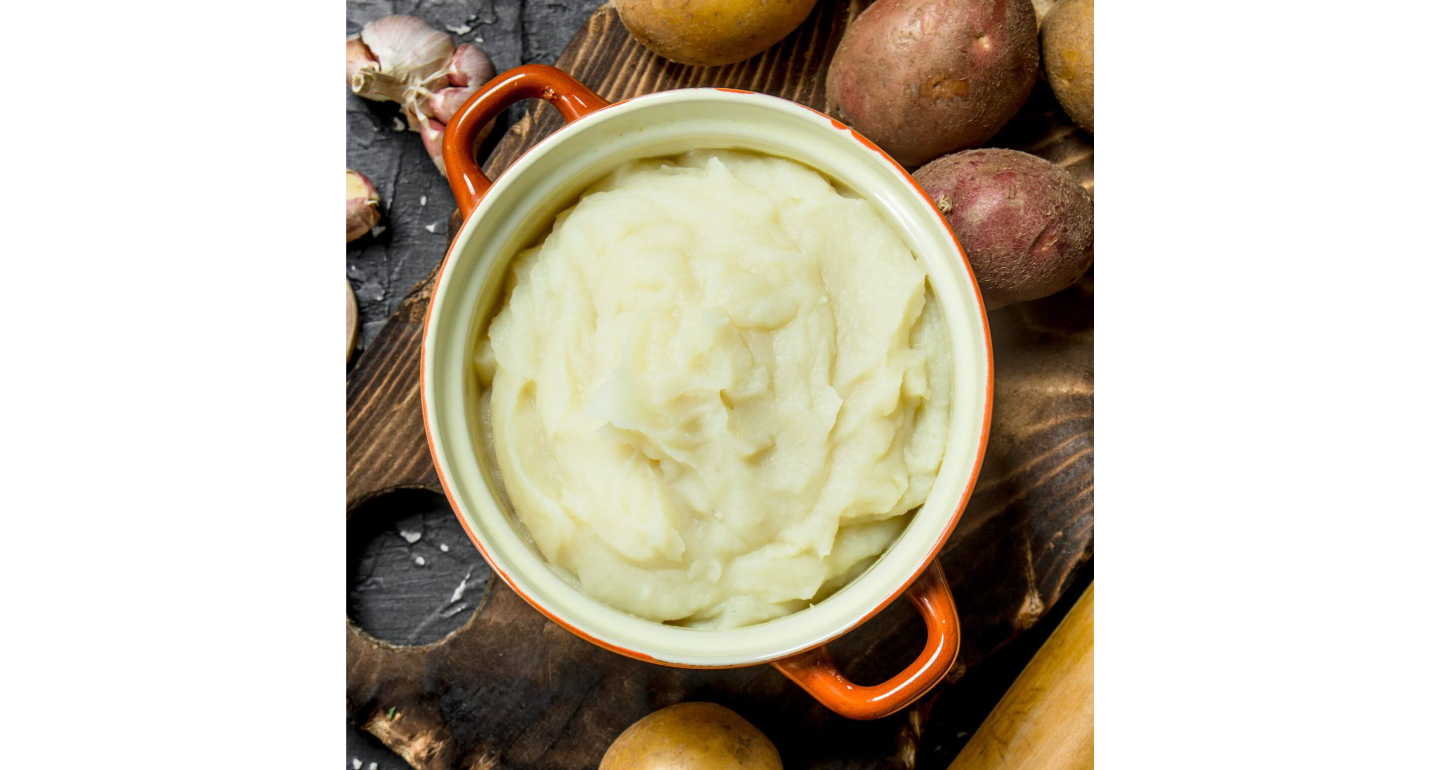 An orange dutch oven resting on a wooden cutting board filled with whipped potatoes.