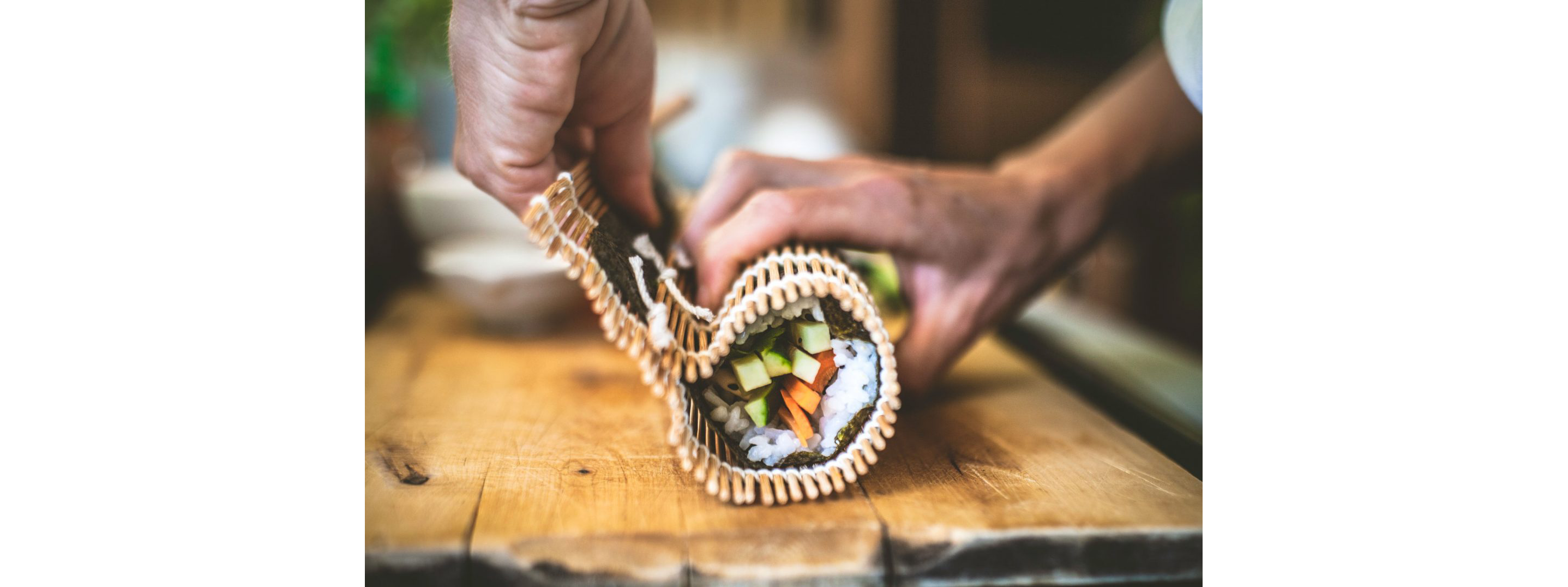 A person delicately rolling a whole roll of sushi with a bamboo rolling mat.