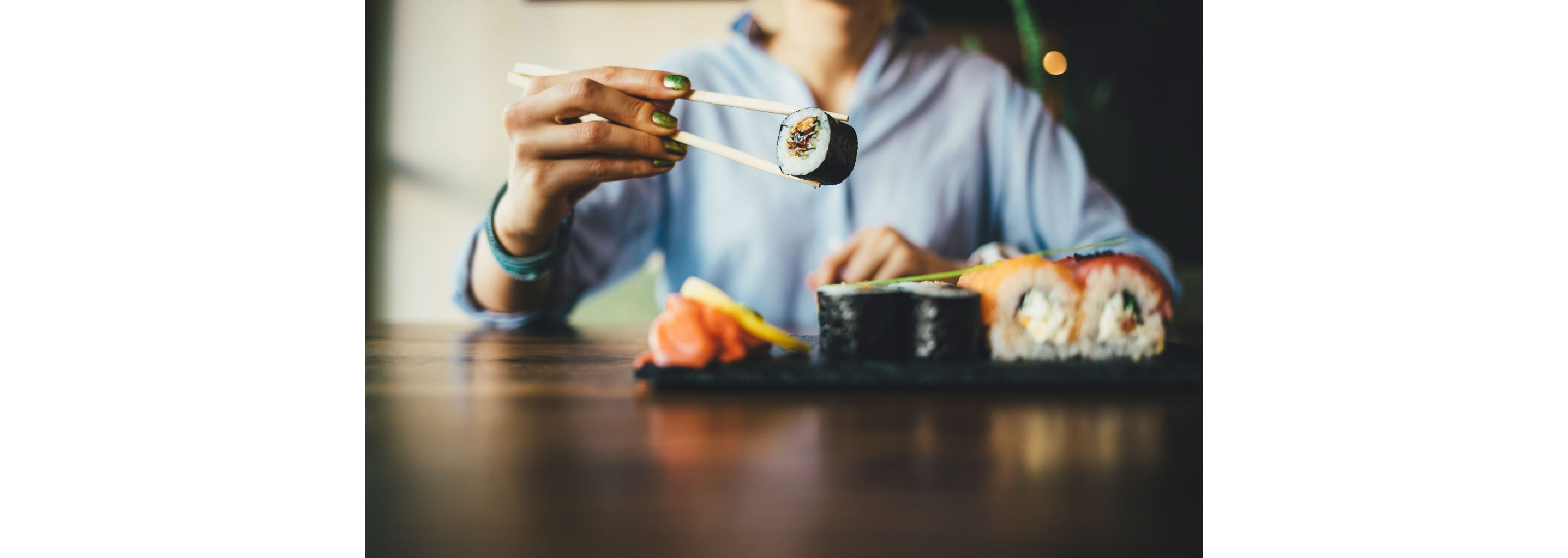 A person holding an individual roll of sushi with a pair of chopsticks.