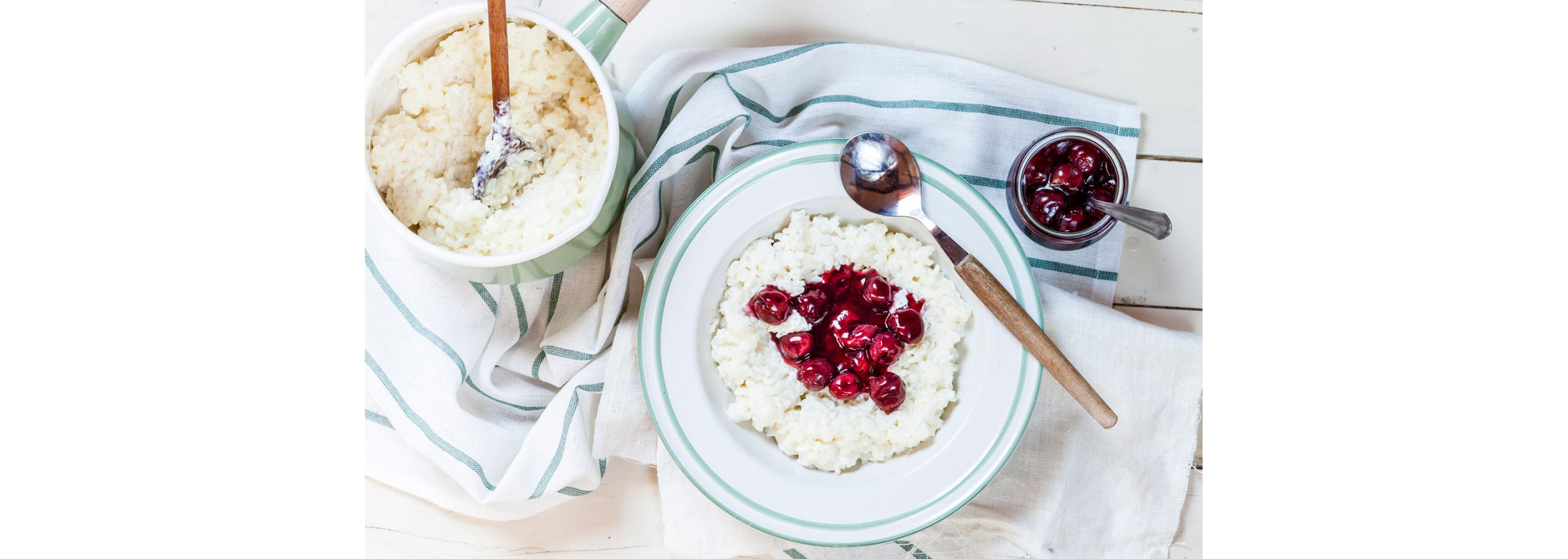 A white bowl with teal trim filled with Risalamande topped with cherry sauce.