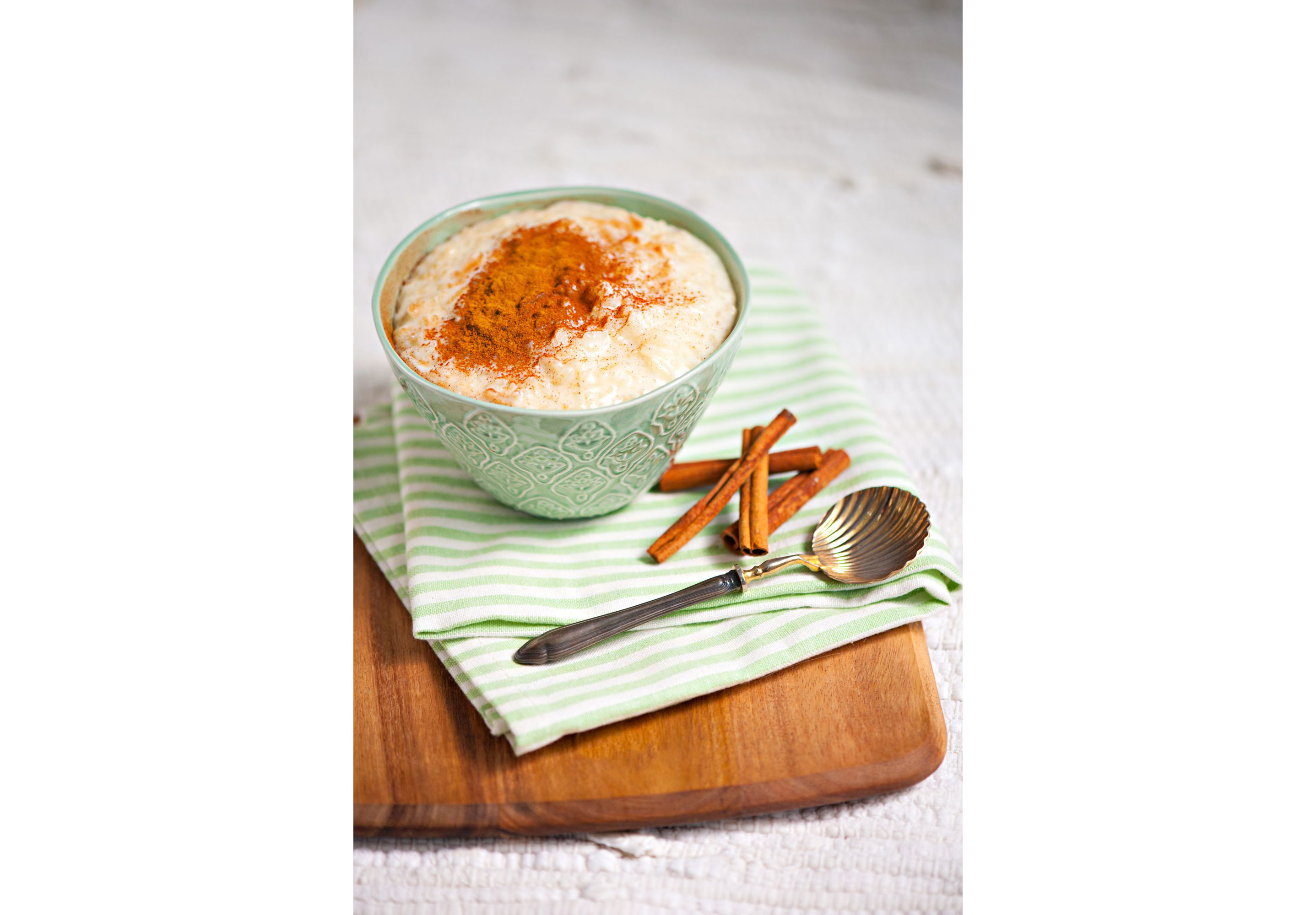 Rice pudding sprinkled with cinnamon in a intricate green bowl.