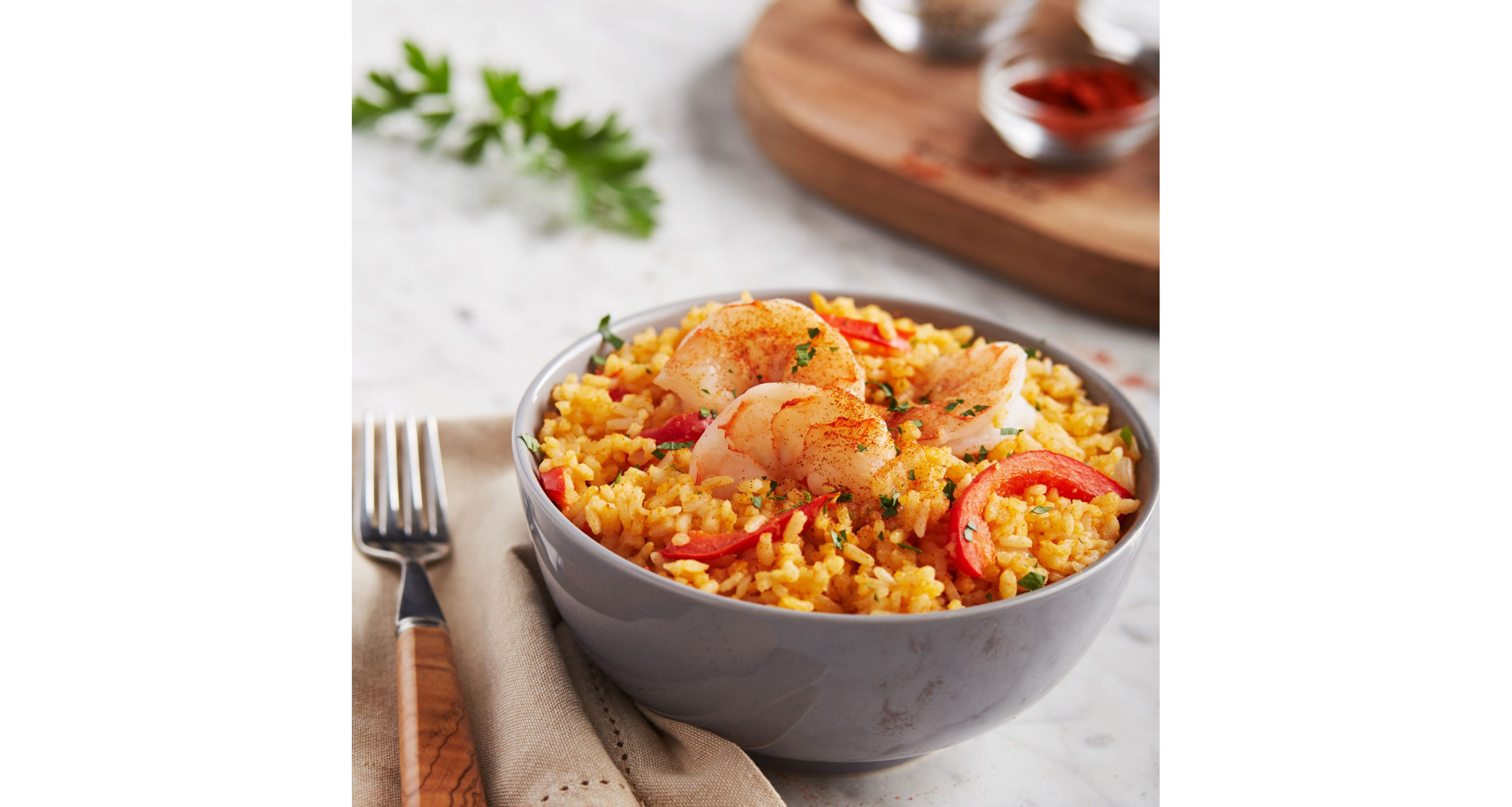 A gray bowl filled with Mexican rice with red bell pepper and cooked shrimps.