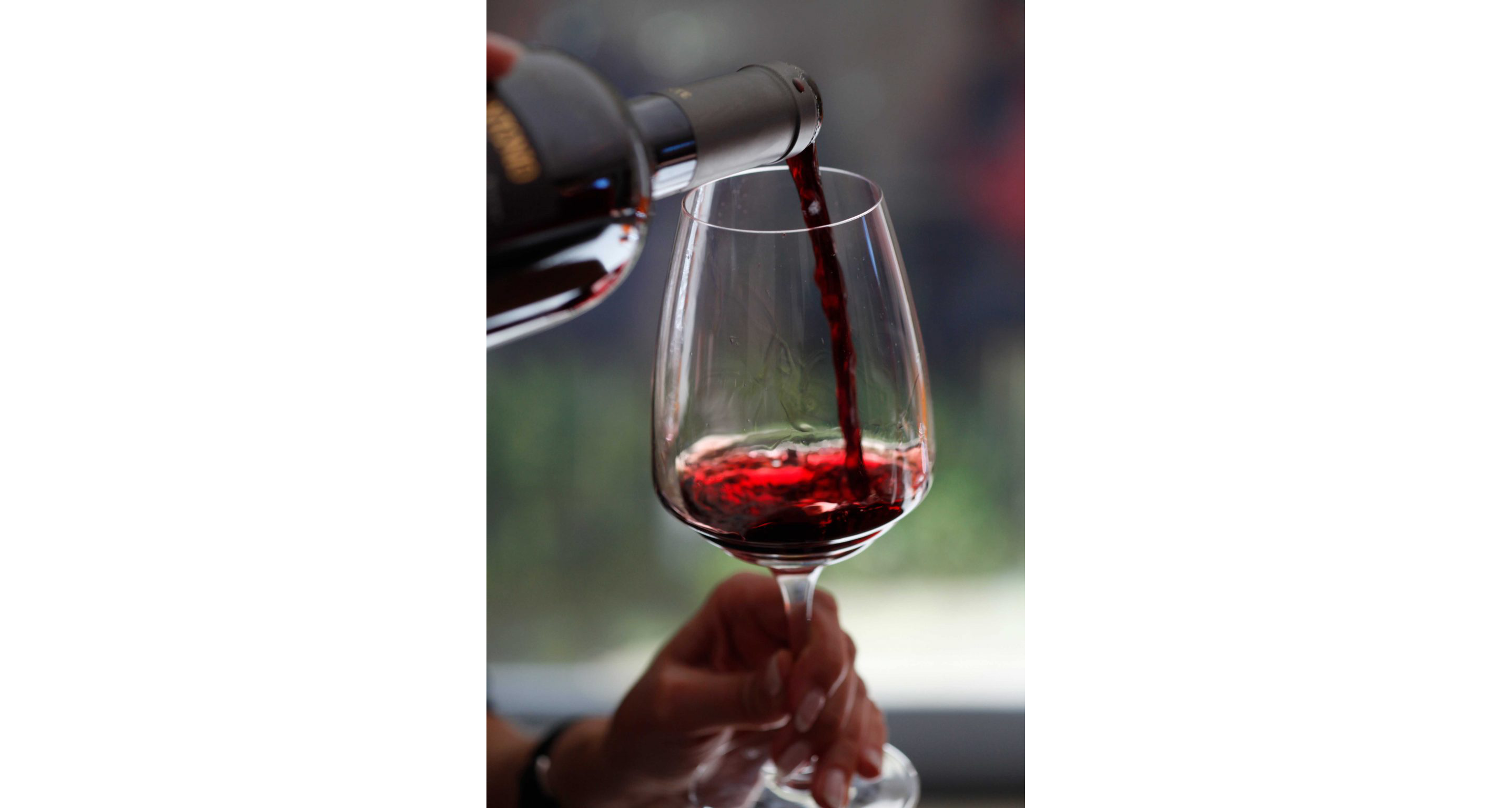 A person filling a clean, clear wine glass with red wine.