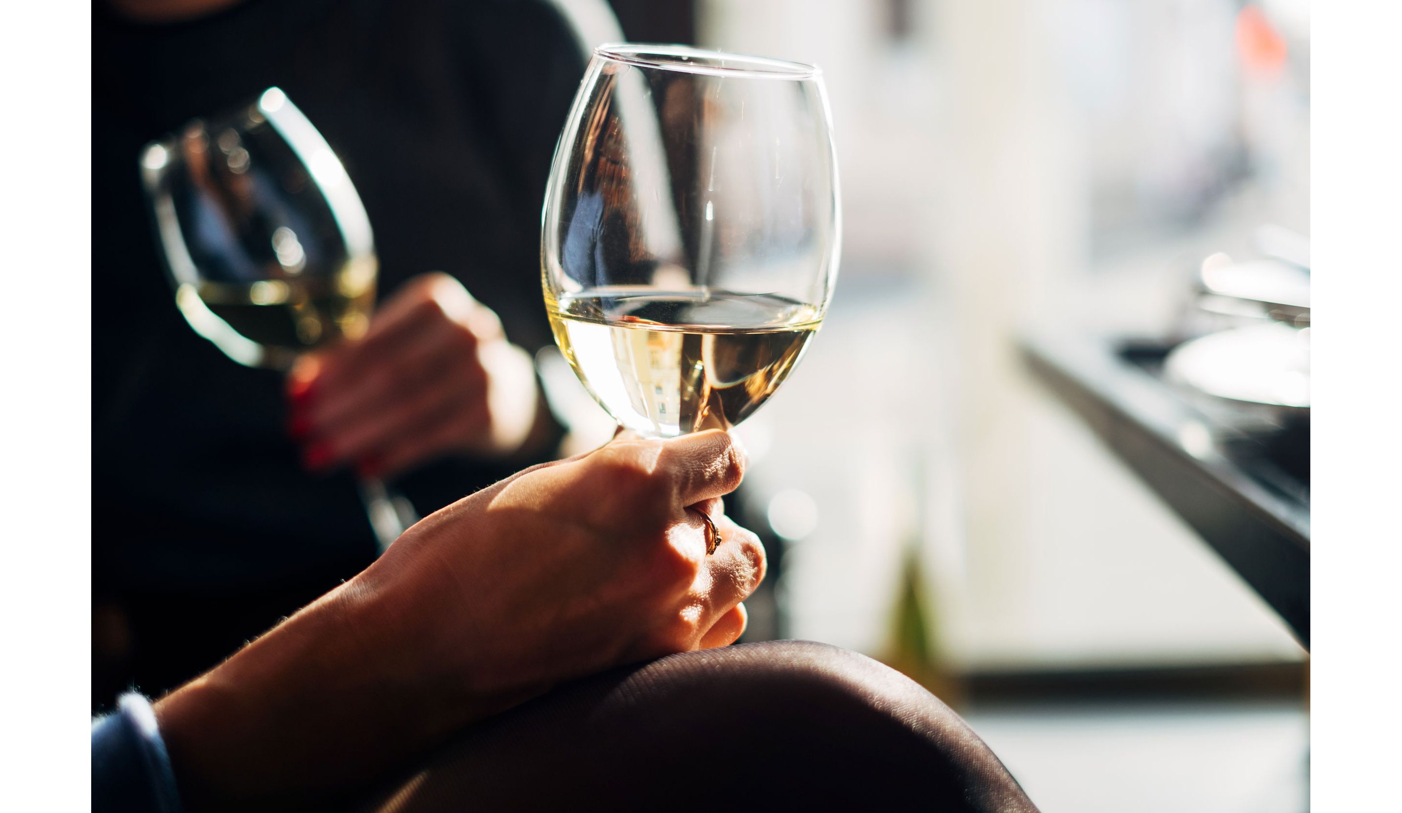 A person holding a clear glass of white wine in the sunlight.