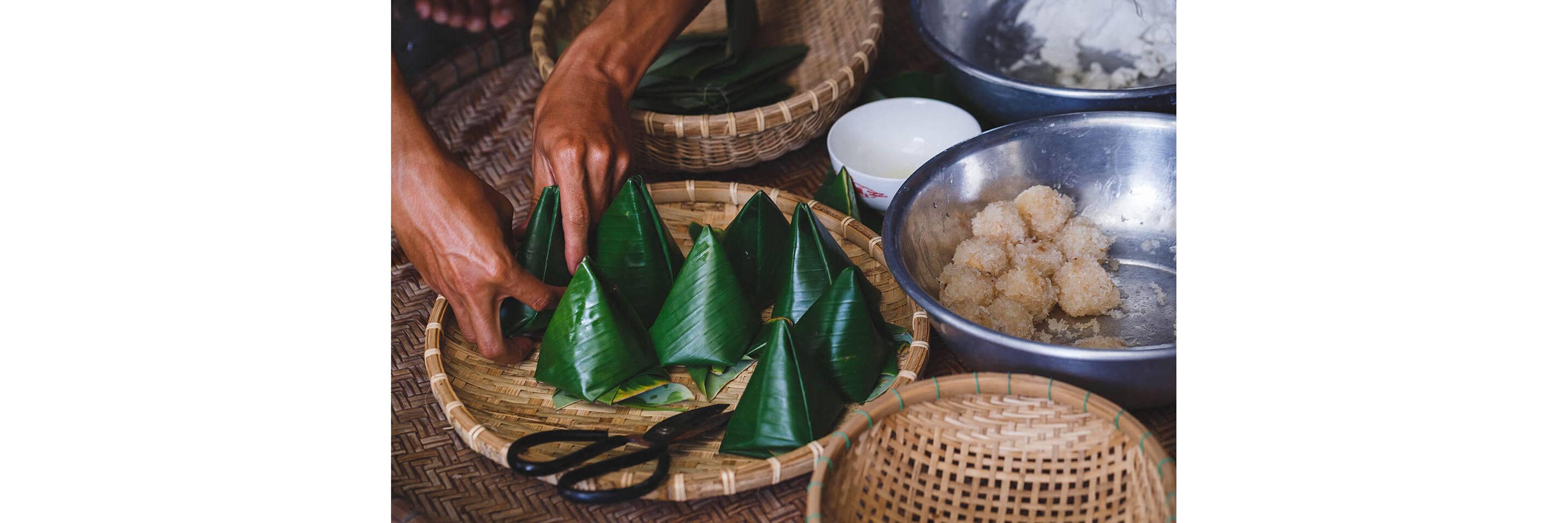 Bundles of food wrapped in vibrant bamboo leaves in a large woven basket.