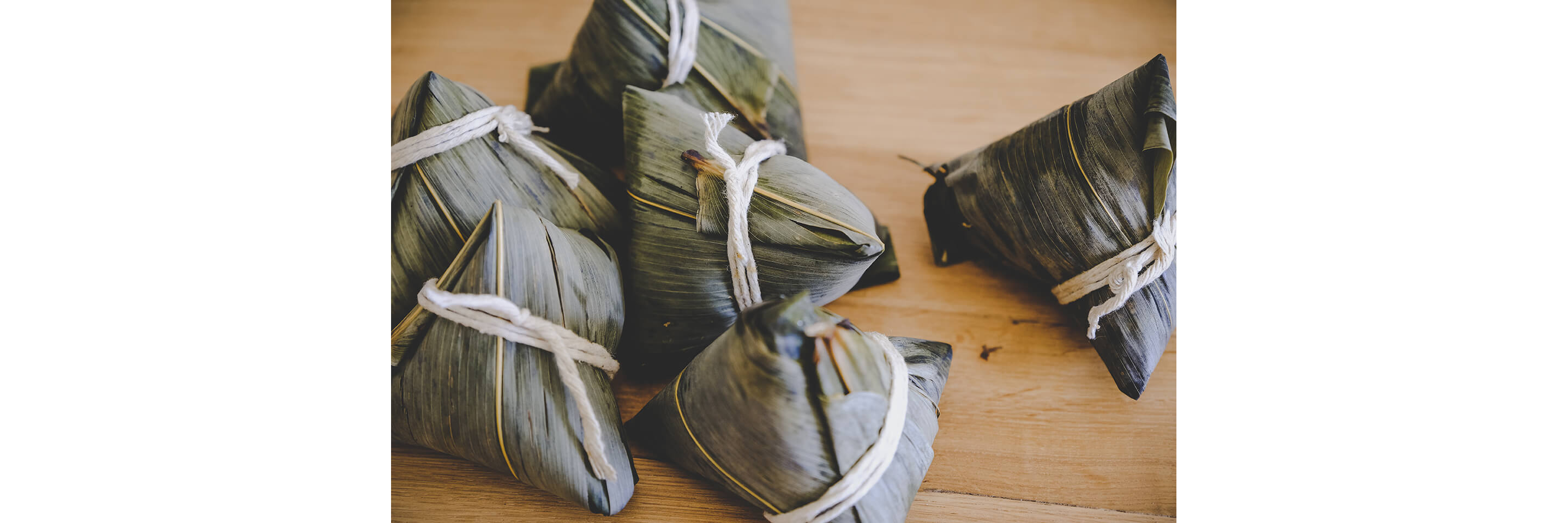 Bundles of food wrapped in bamboo leaves tied shut with twine.