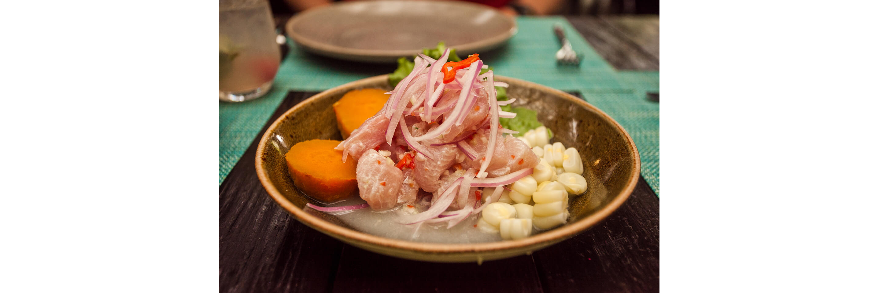 A dark bowl filled with freshly made ceviche topped with sliced red onions.