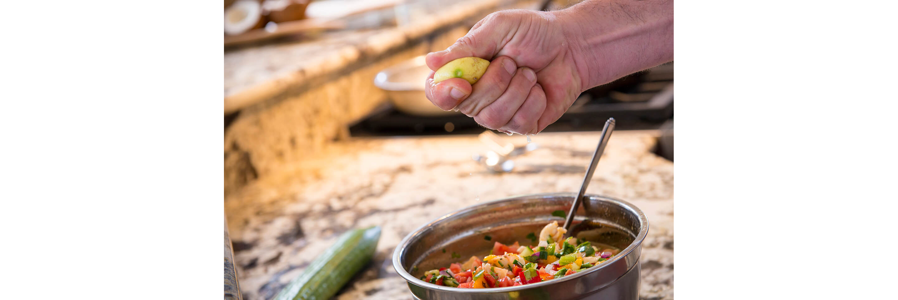 A person squeezing lemon into a silver bowl of ceviche.