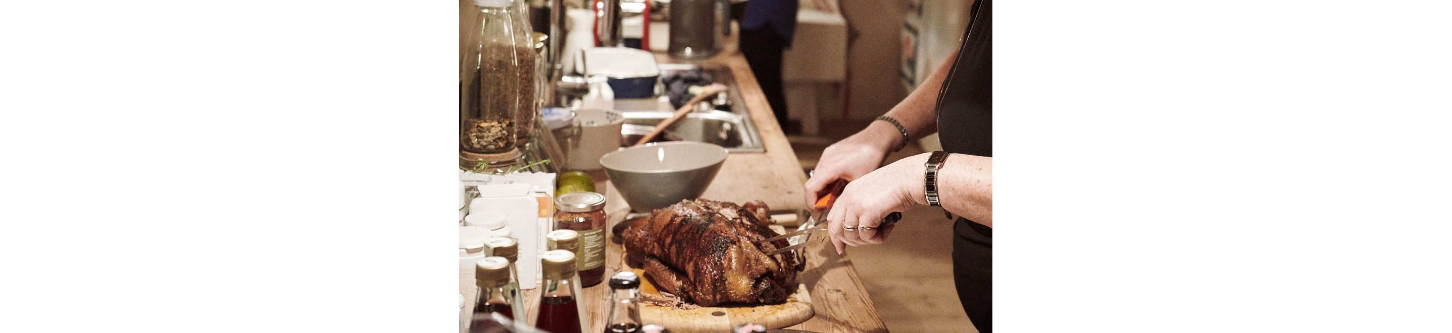 A person slicing a roasted duck on a wooden cutting board.