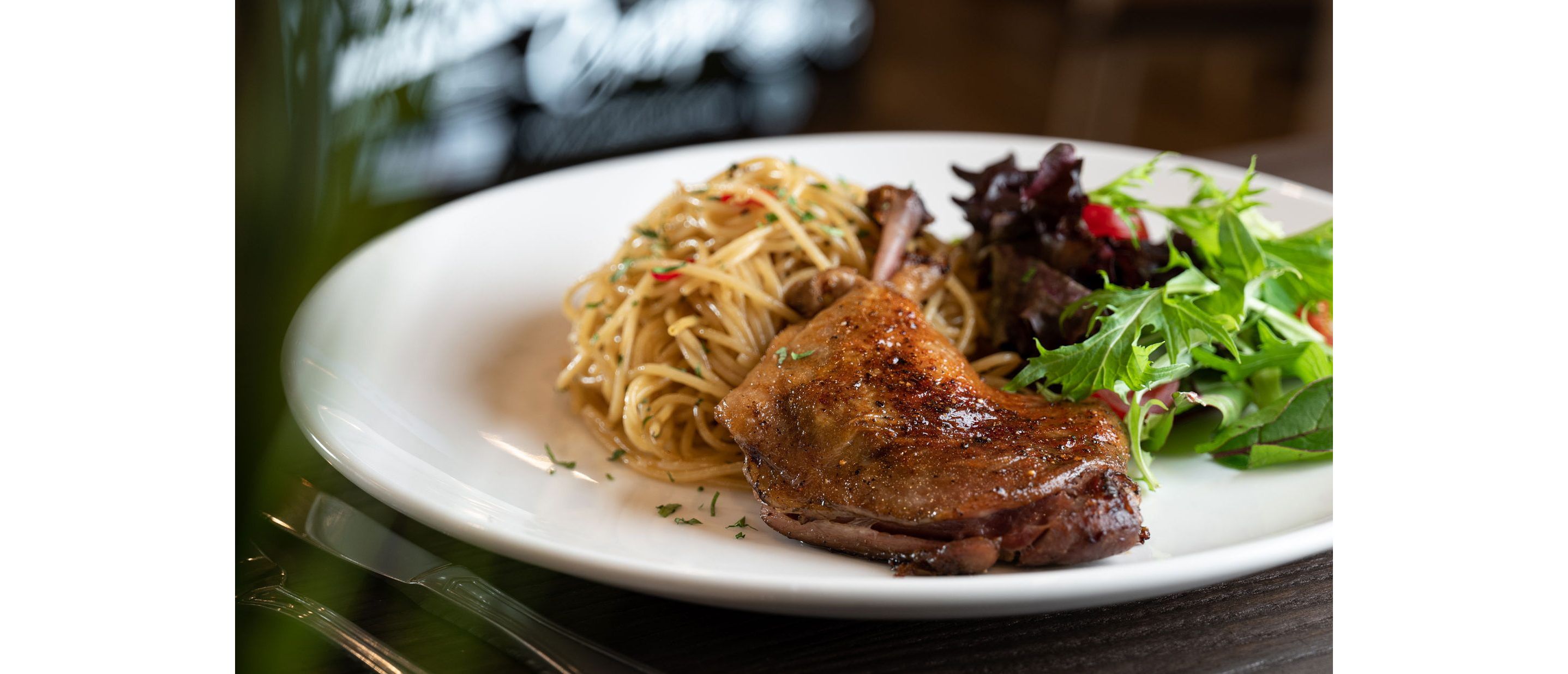 A white dinner plate filled with duck, spaghetti and salad.