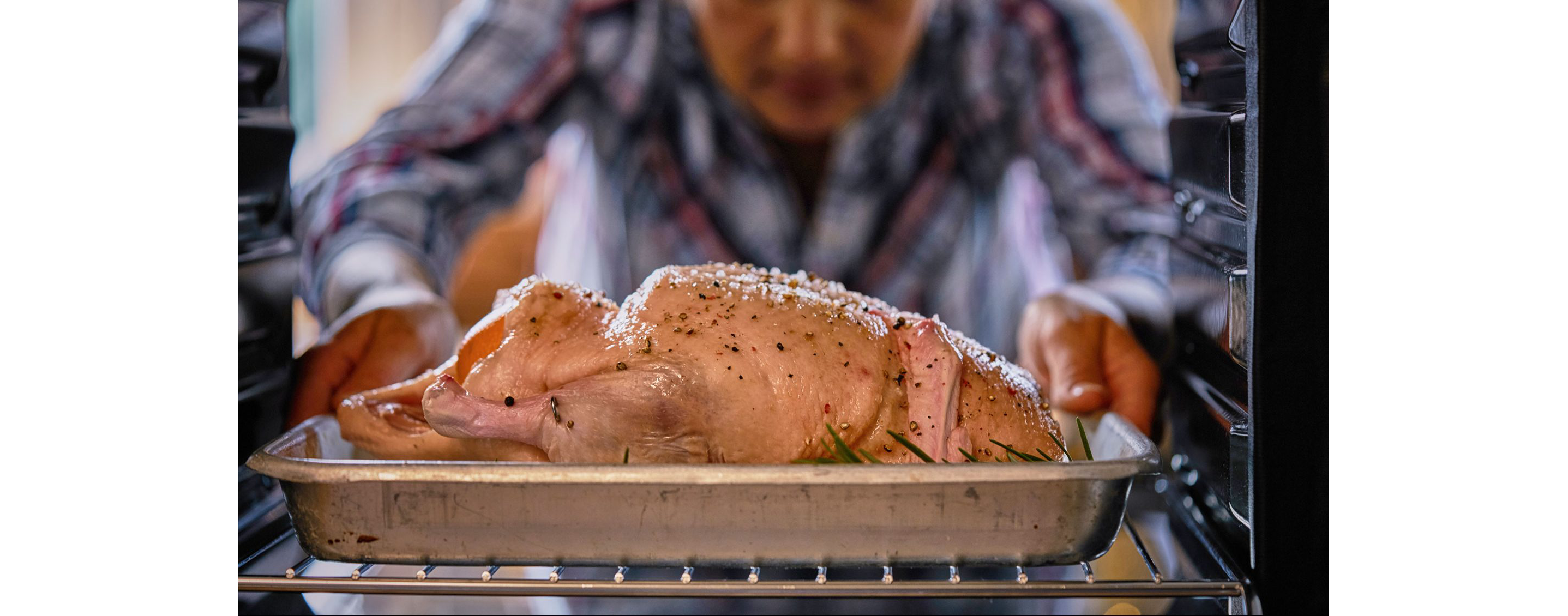 A person placing a whole duck in the oven to be roasted.
