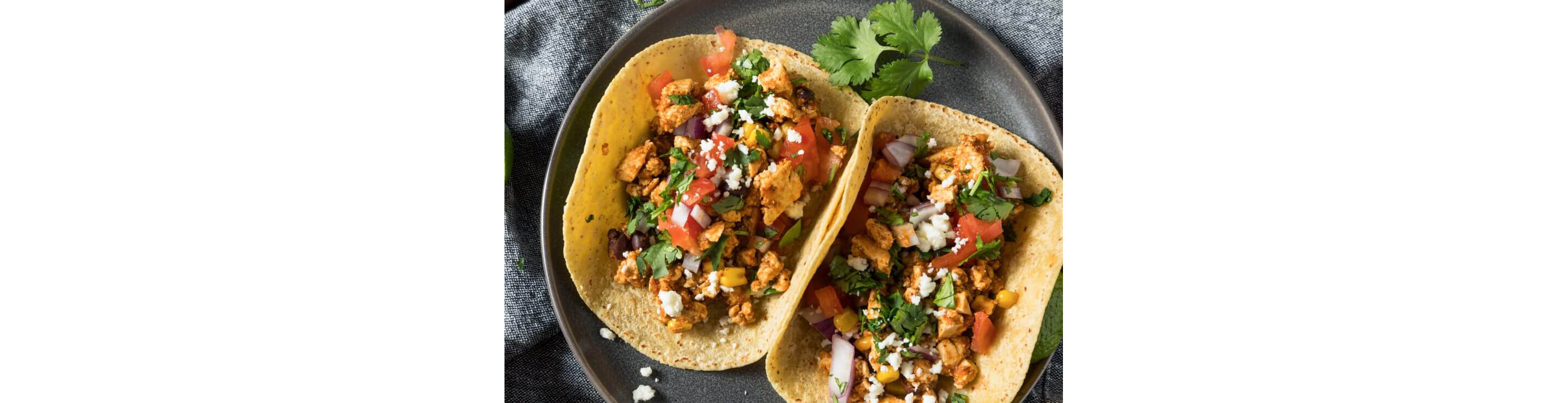 A plate of two chicken tacos topped with cilantro, tomato and onion garnished with queso fresco.