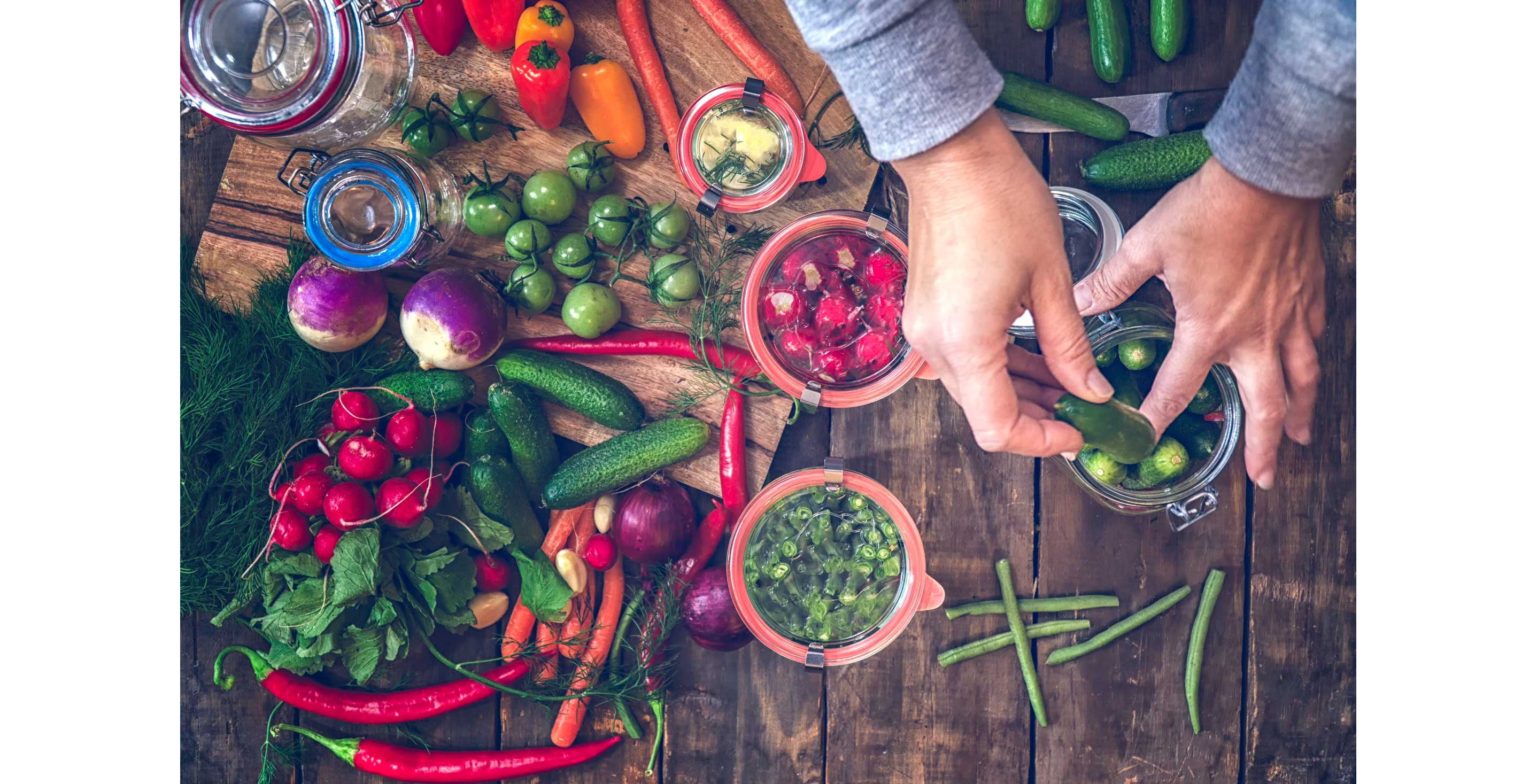 A variety of colorful vegetables strewn about the table to be pickled in glass jars.