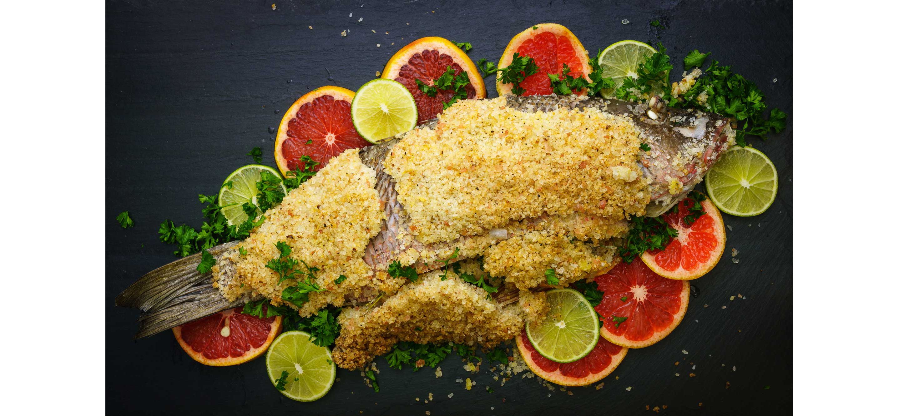 A salt-crusted sea bass resting atop thinly sliced citruses.