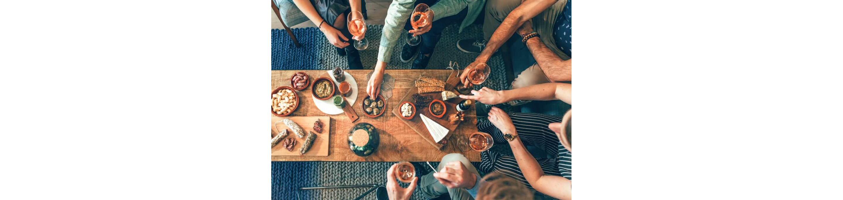 A gathering of friends sitting around a coffee table sharing small eats and sipping wine.