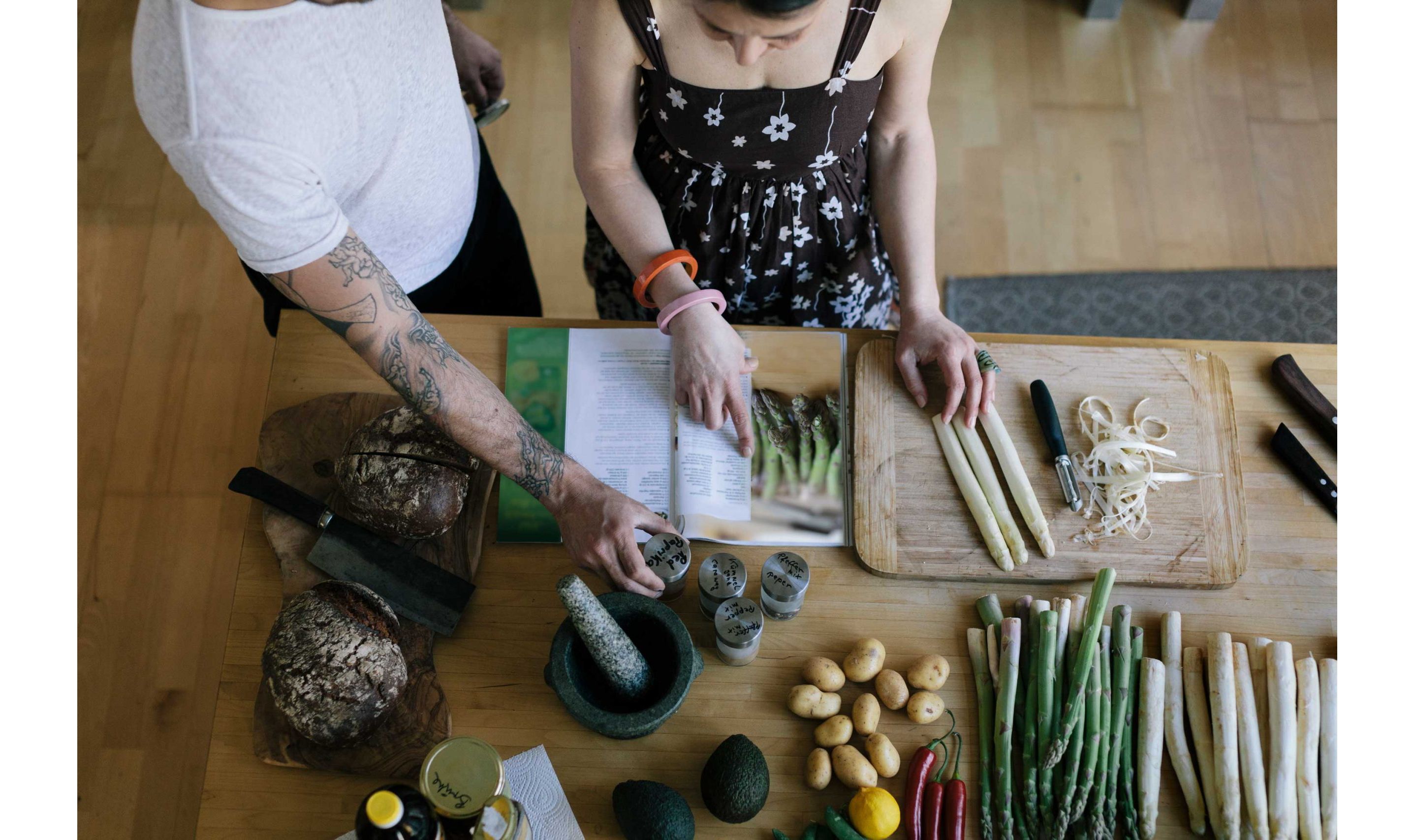 Two people reading through an asparagus recipe in a cook book together.
