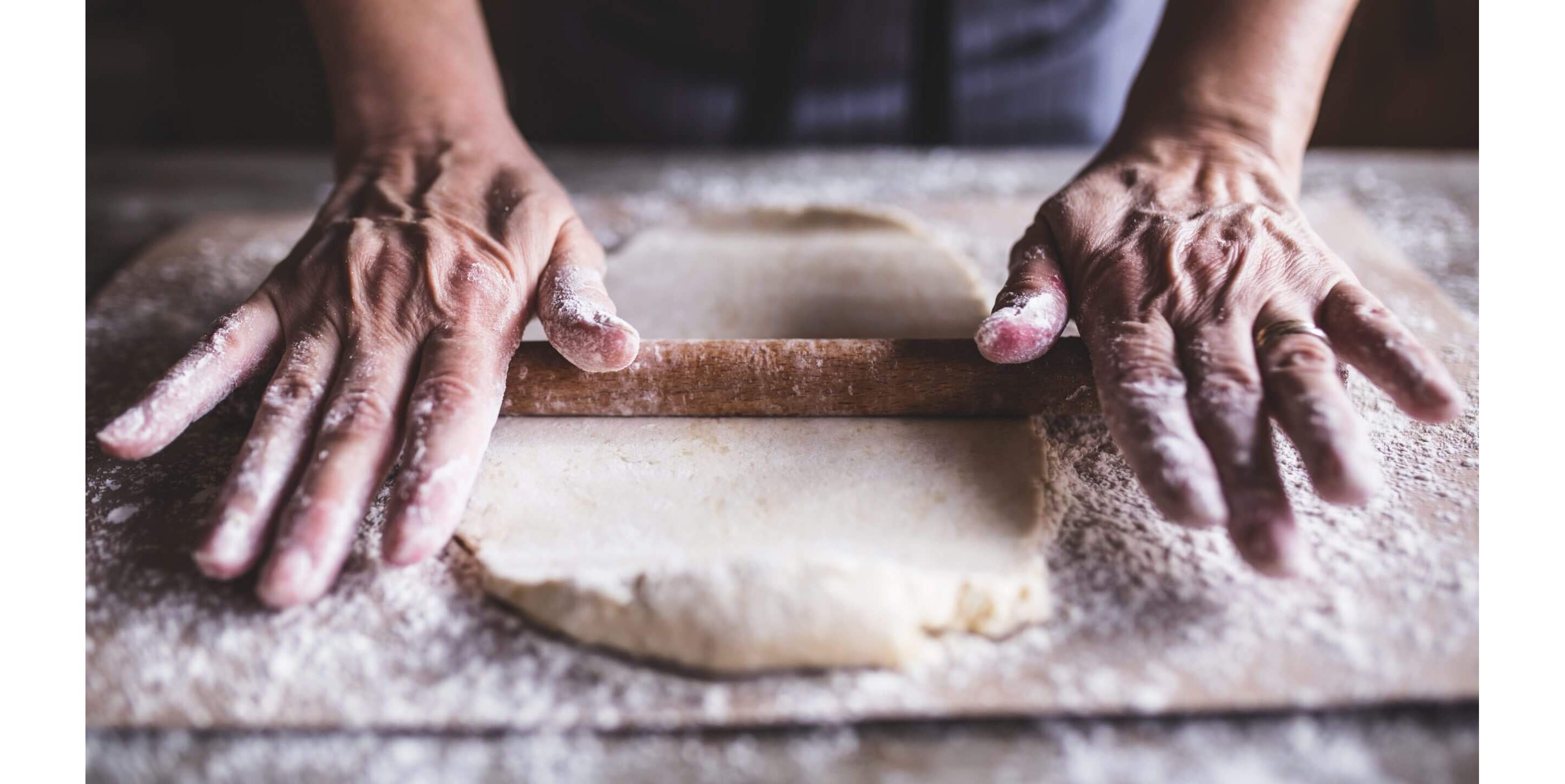 Strong hands masterfully rolling dough covered in flour on a wooden cutting board.