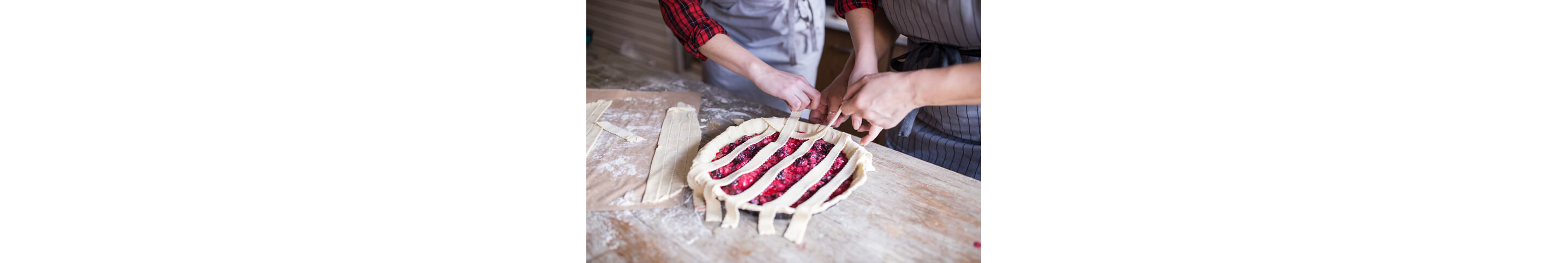 Two people weaving thinly sliced, rolled out dough into an intricate pie crust.